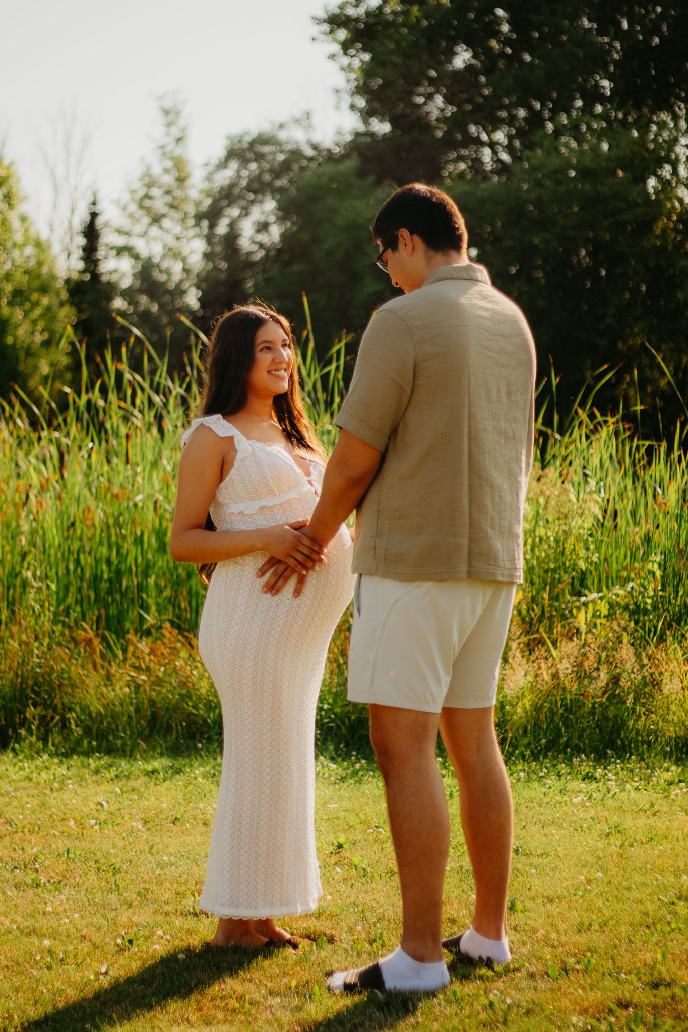 Playful maternity photos of a couple in coordinated white and beige outfits in a summer field.