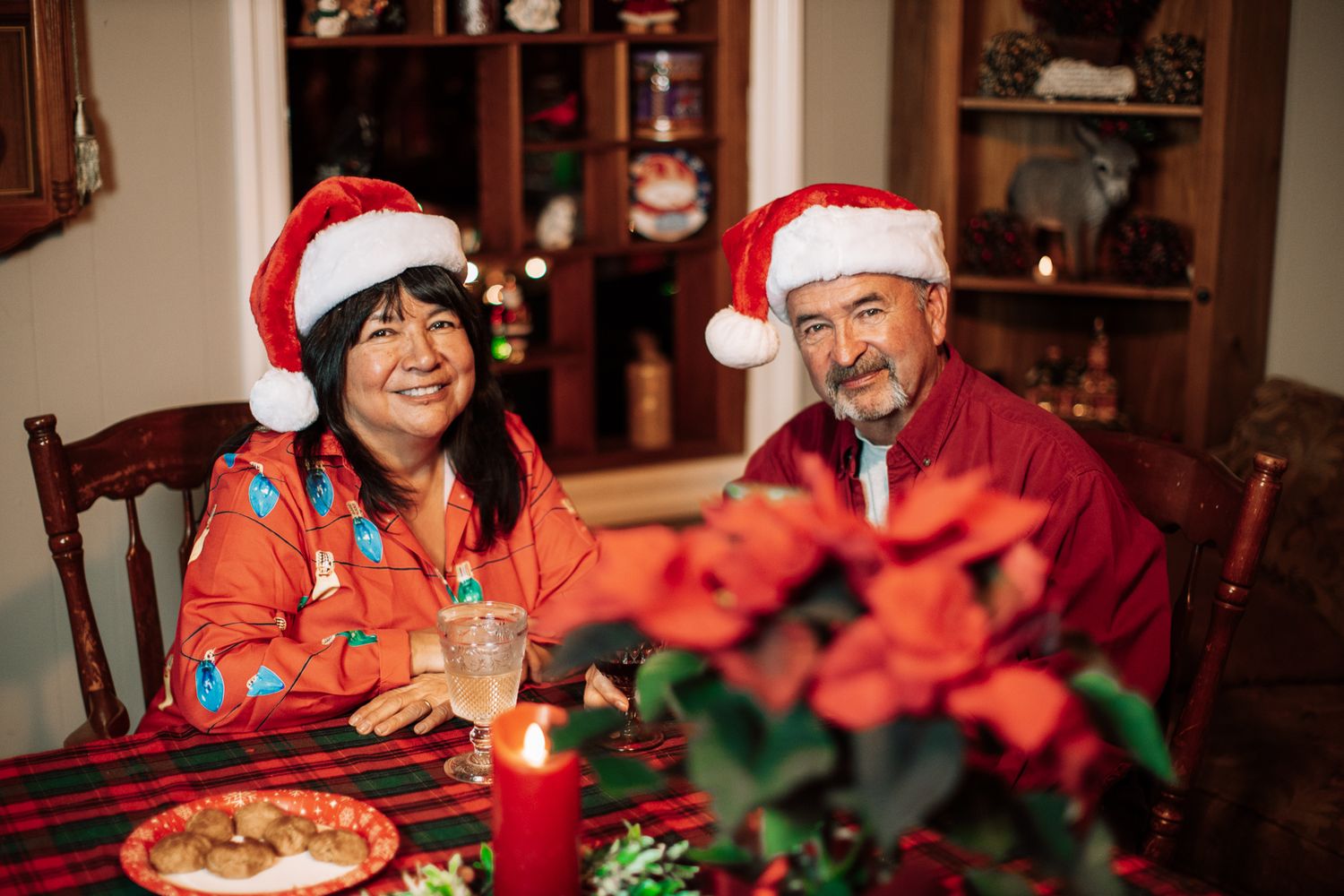 Holiday gathering around a table with Santa hats and red poinsettia decorations.