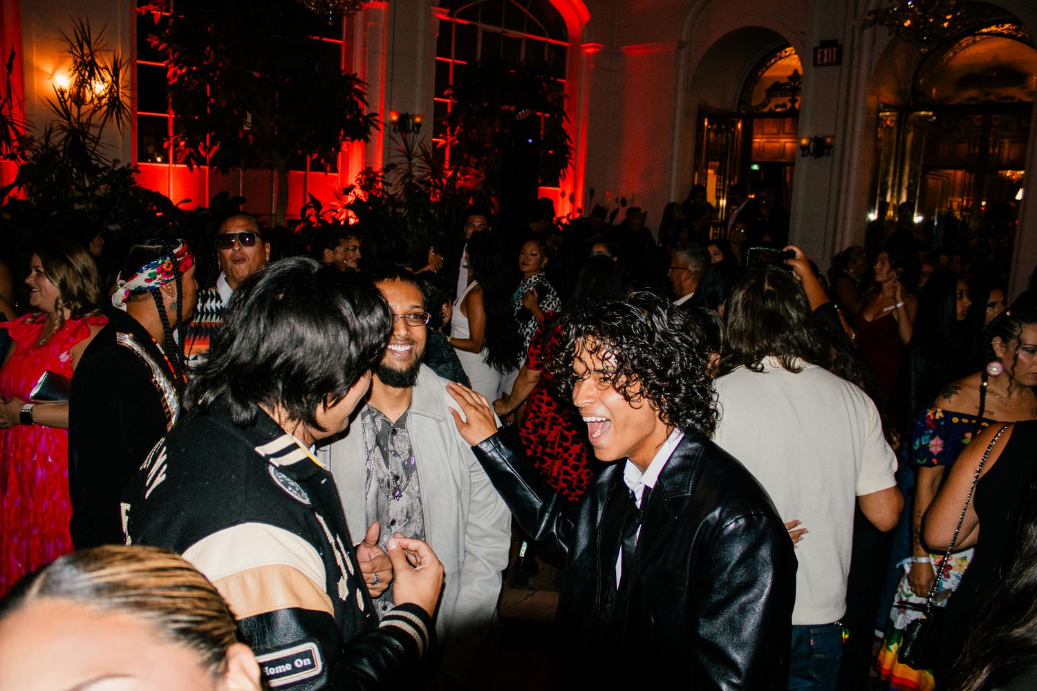 Crowded evening event with red ambient lighting and guests mingling in a large venue.