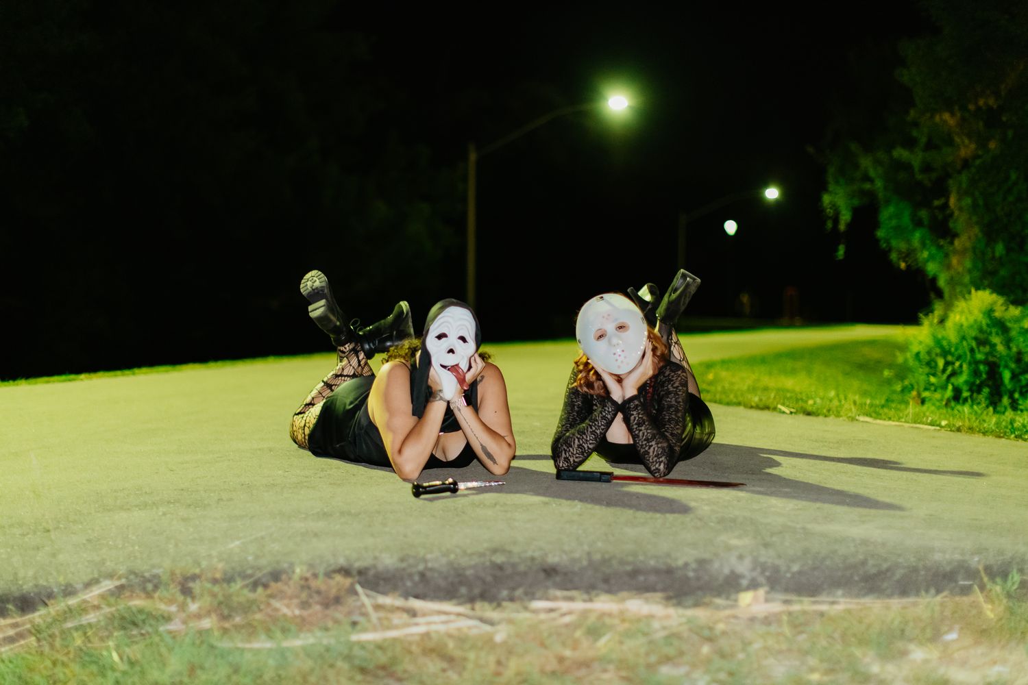 Masked figures lying on ground in nighttime parking lot under streetlights.