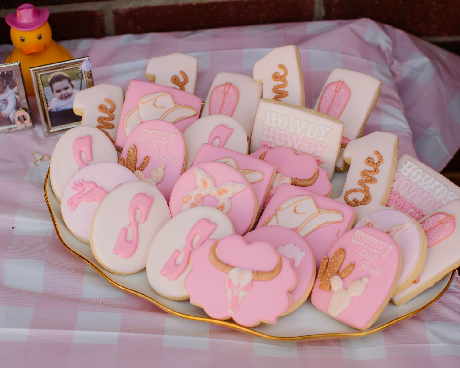 Pink and gold cowgirl themed sugar cookies on a plate for a first birthday party.