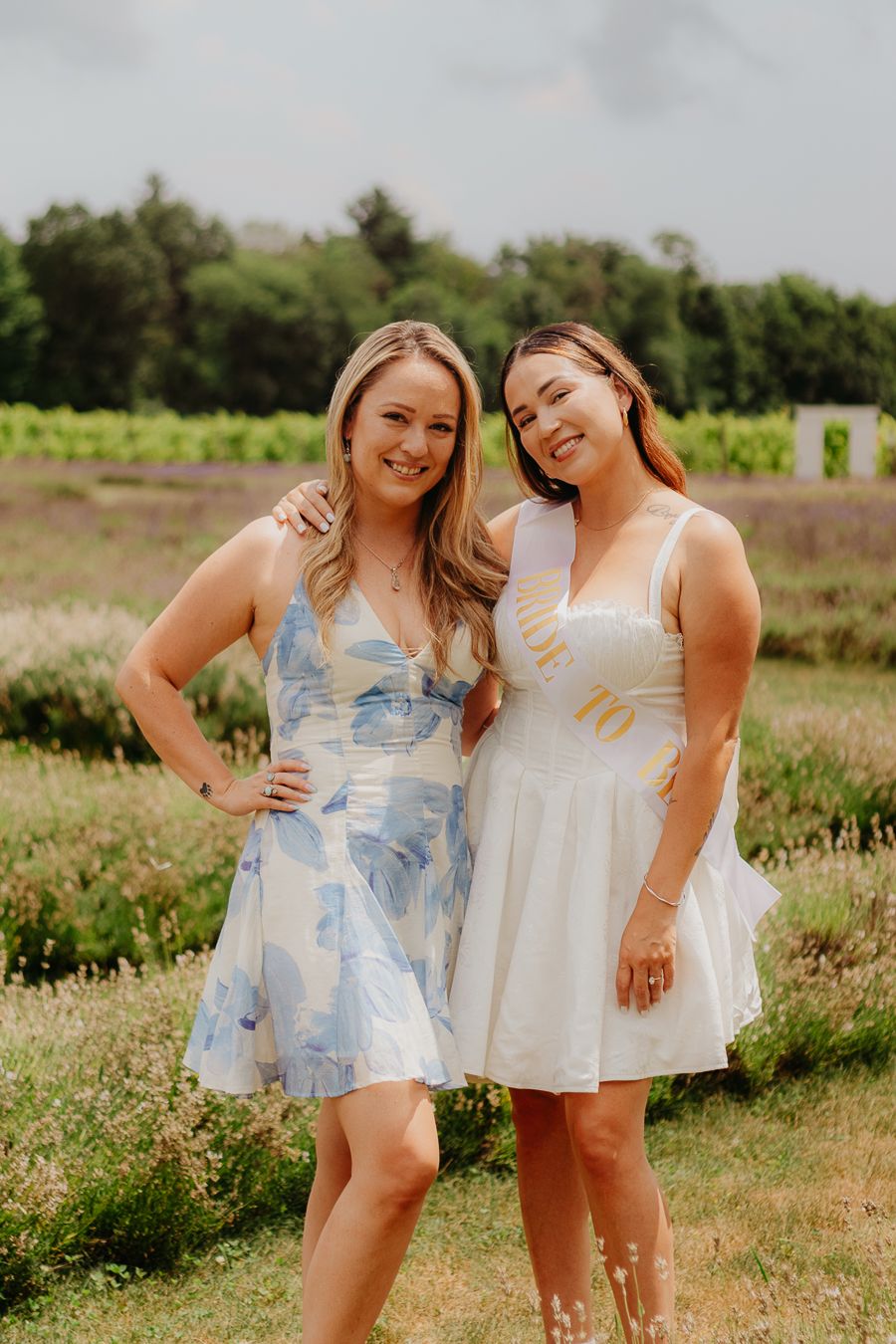 Two friends in summer dresses laughing together in a sunny field.