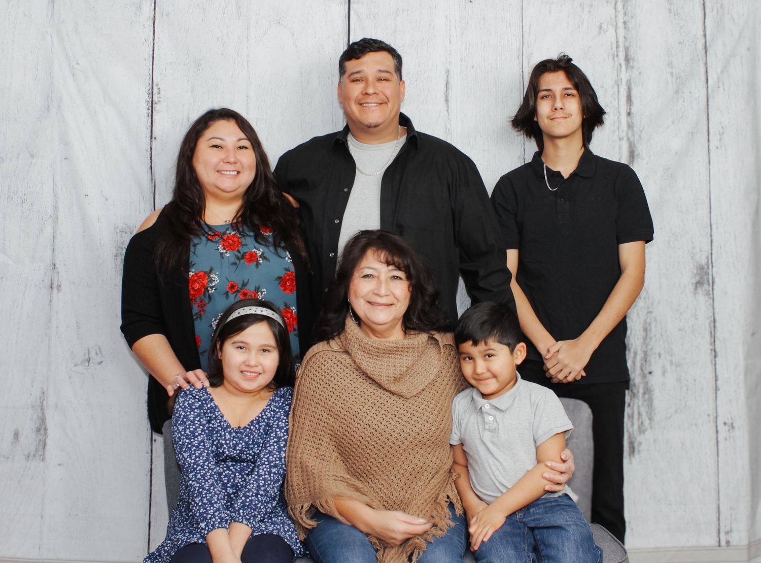 Casual family group photo with multiple members against light backdrop.