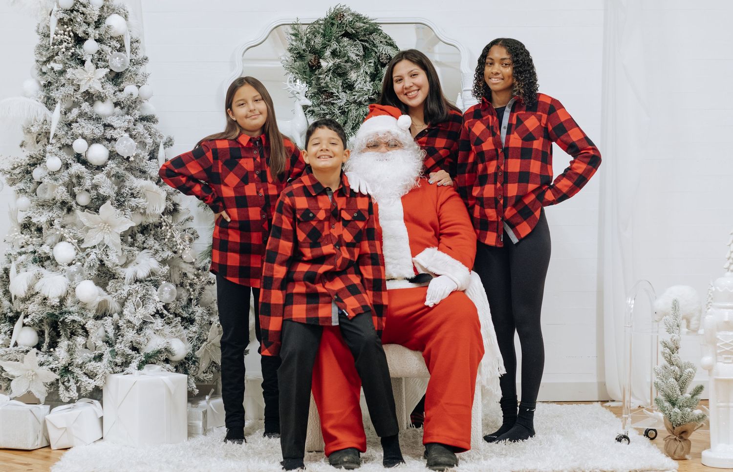 Group wearing festive buffalo plaid outfits poses in front of white Christmas trees and holiday decor.