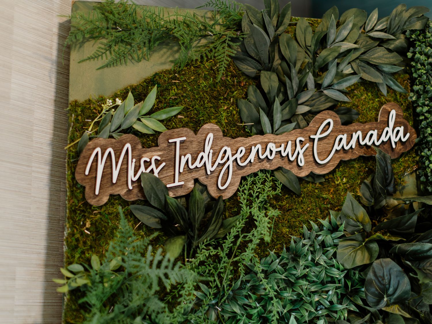 Decorative moss wall art sign reading Miss Indigenous Canada surrounded by lush green ferns and foliage.