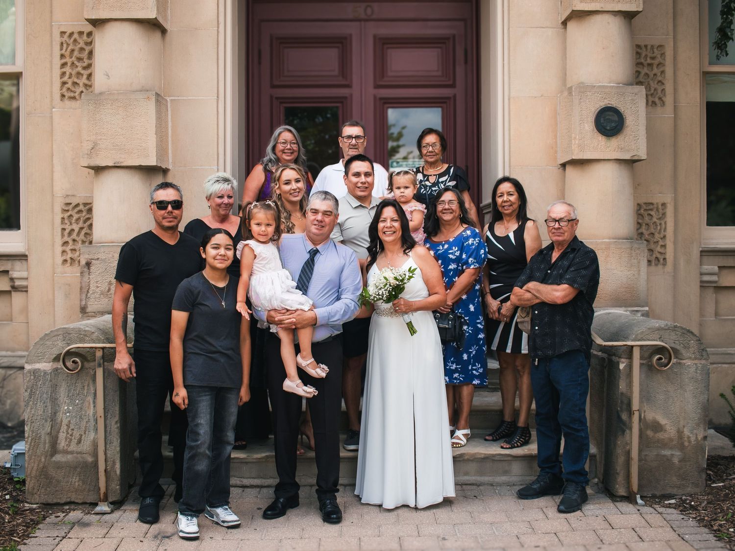 Wedding party and guests posed together on stone steps of a building.