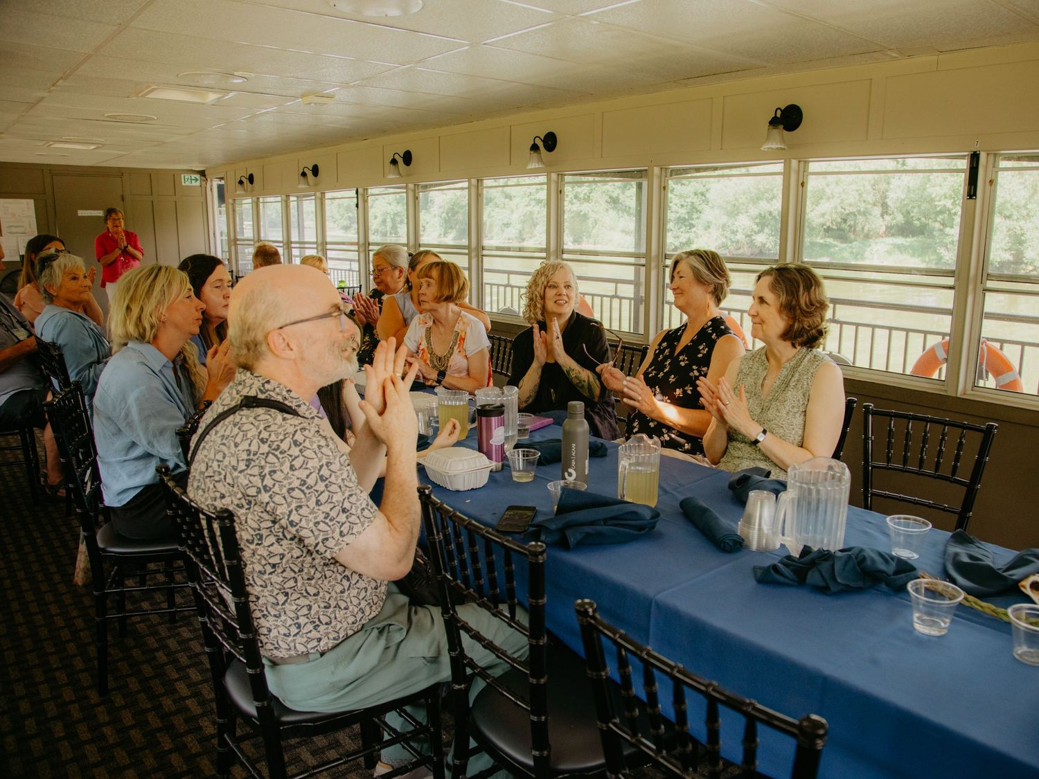 Wedding reception venue with guests seated at tables near large windows.