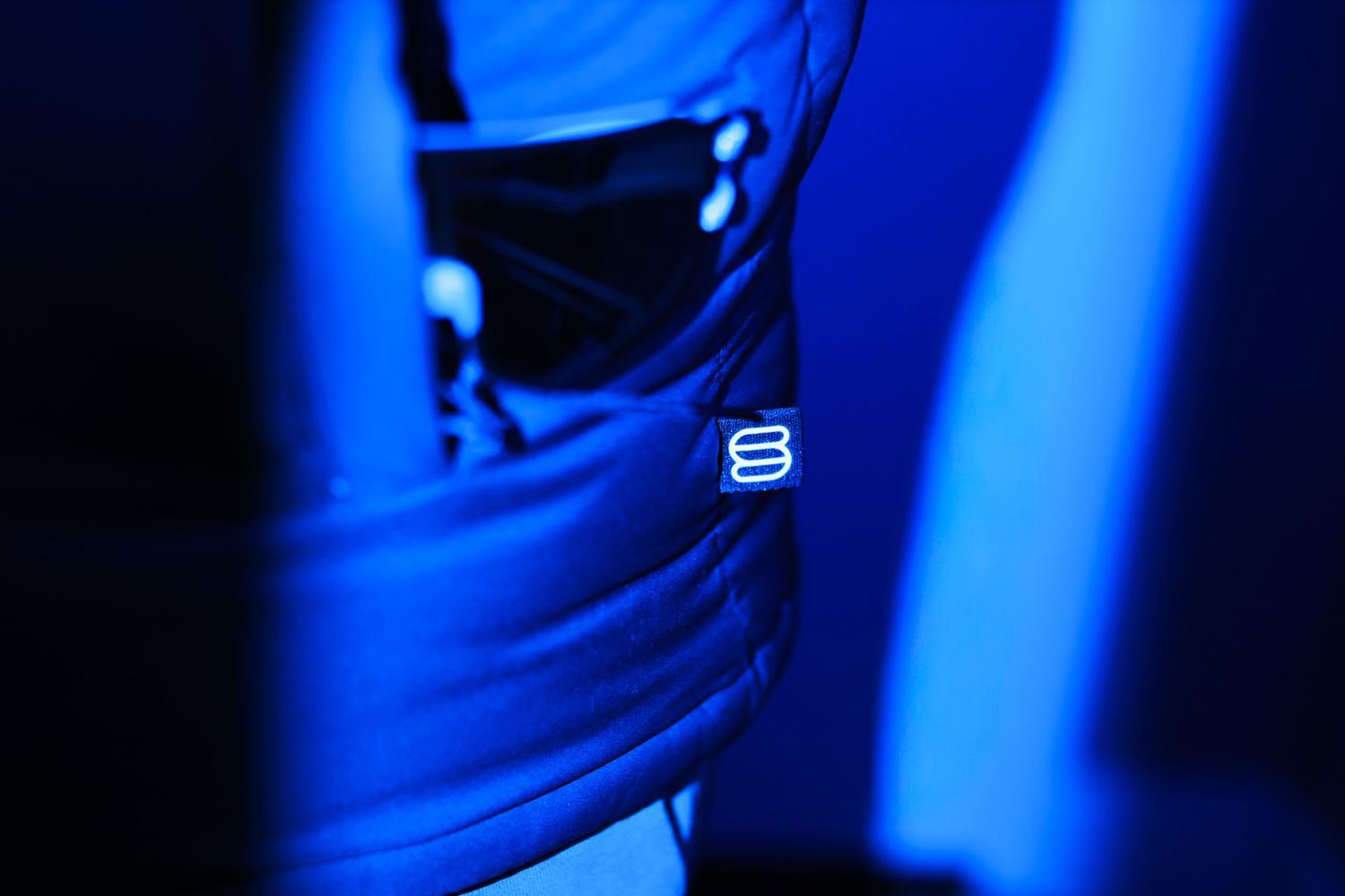 Close-up of a black puffer jacket with glowing logo detail under dramatic blue lighting.