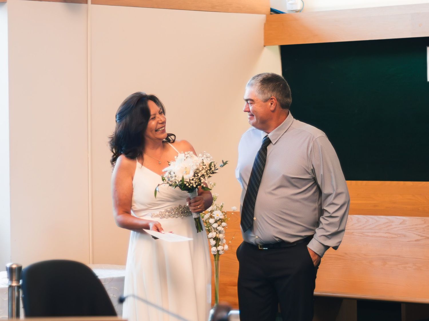 Bride and groom share a smile during intimate civil wedding ceremony in a courtroom setting.