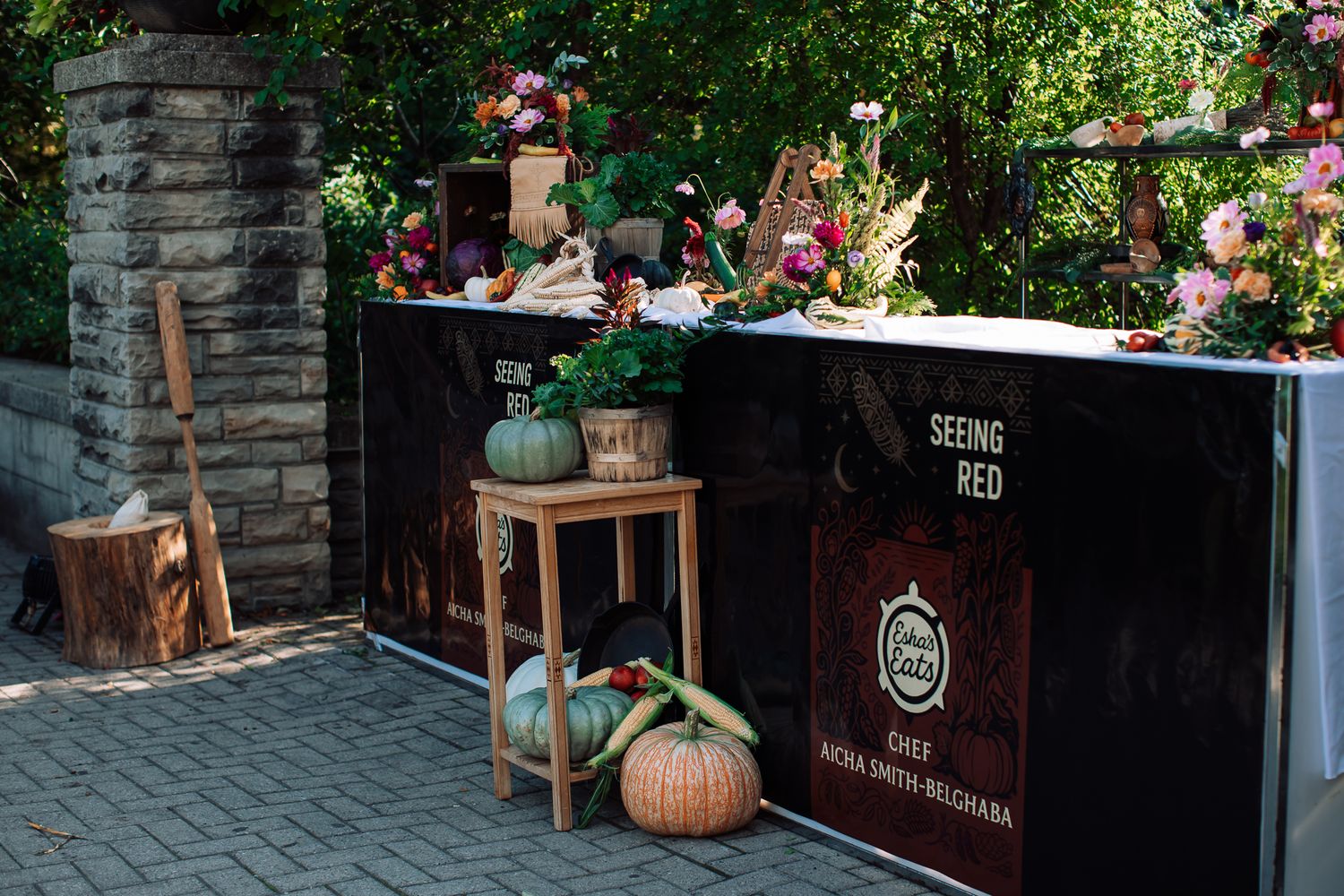 Outdoor cooking station with pumpkins, flowers, and a sign reading Seeing Red by Chef Silvia Smith-Bechara.