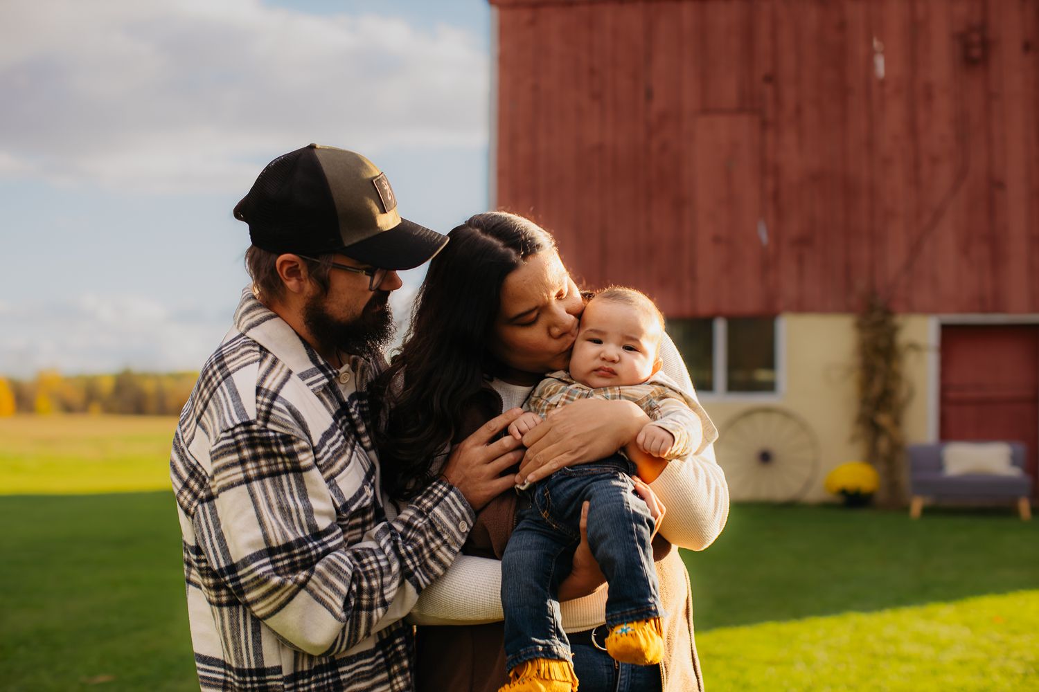 A tender family moment is captured against the backdrop of a red barn on an autumn day.