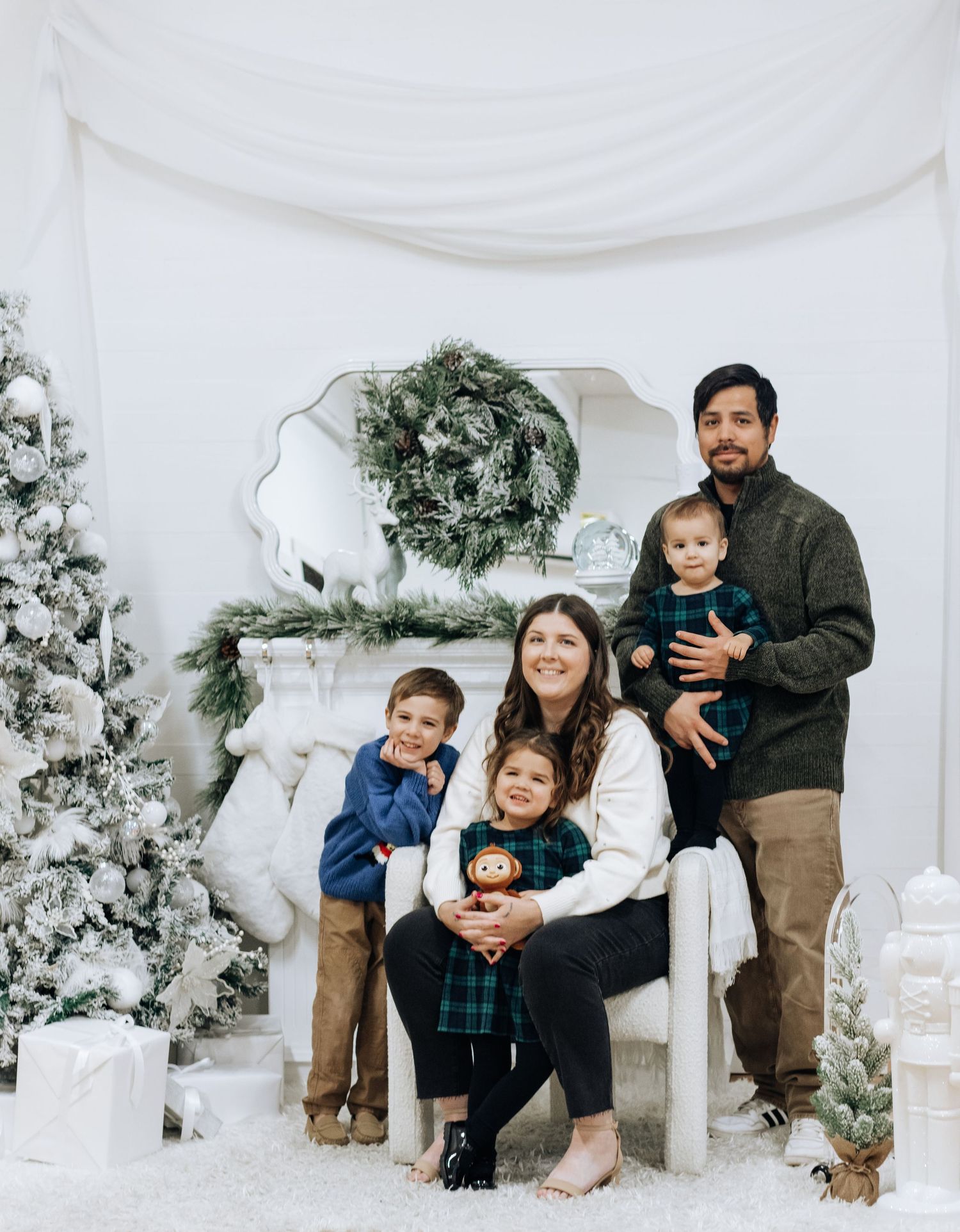 Family poses together in a cozy winter photoshoot setting with white decor and evergreen accents.