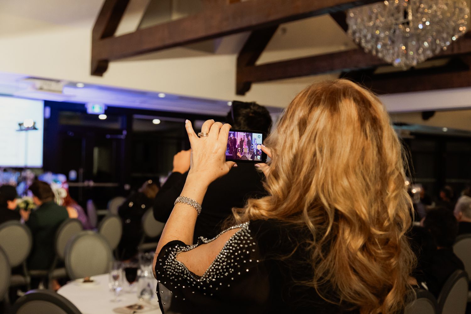 Audience members watching a performance in a decorated banquet hall with purple ambient lighting.