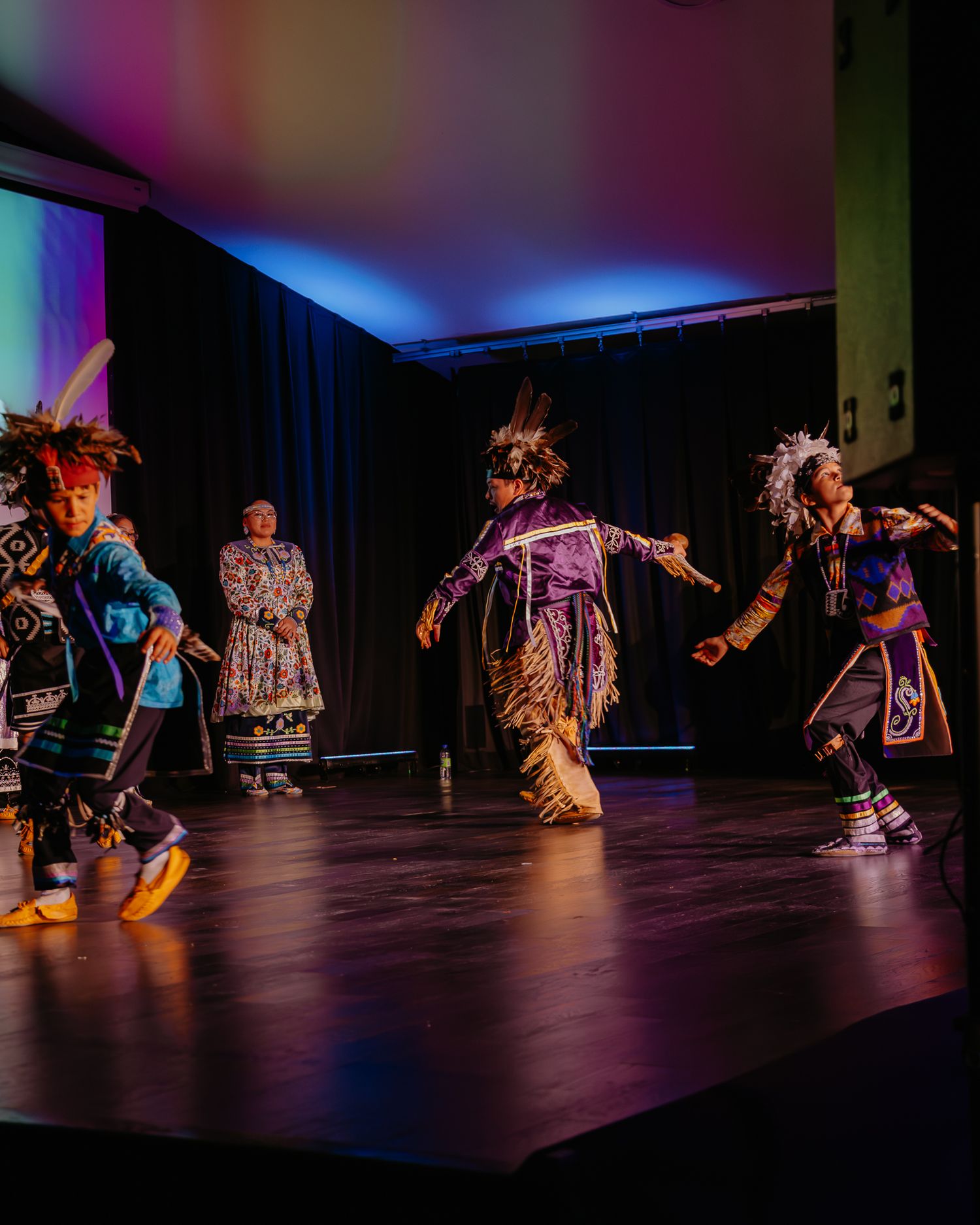 Traditional dancers perform on a dark stage with dramatic lighting during a cultural performance.