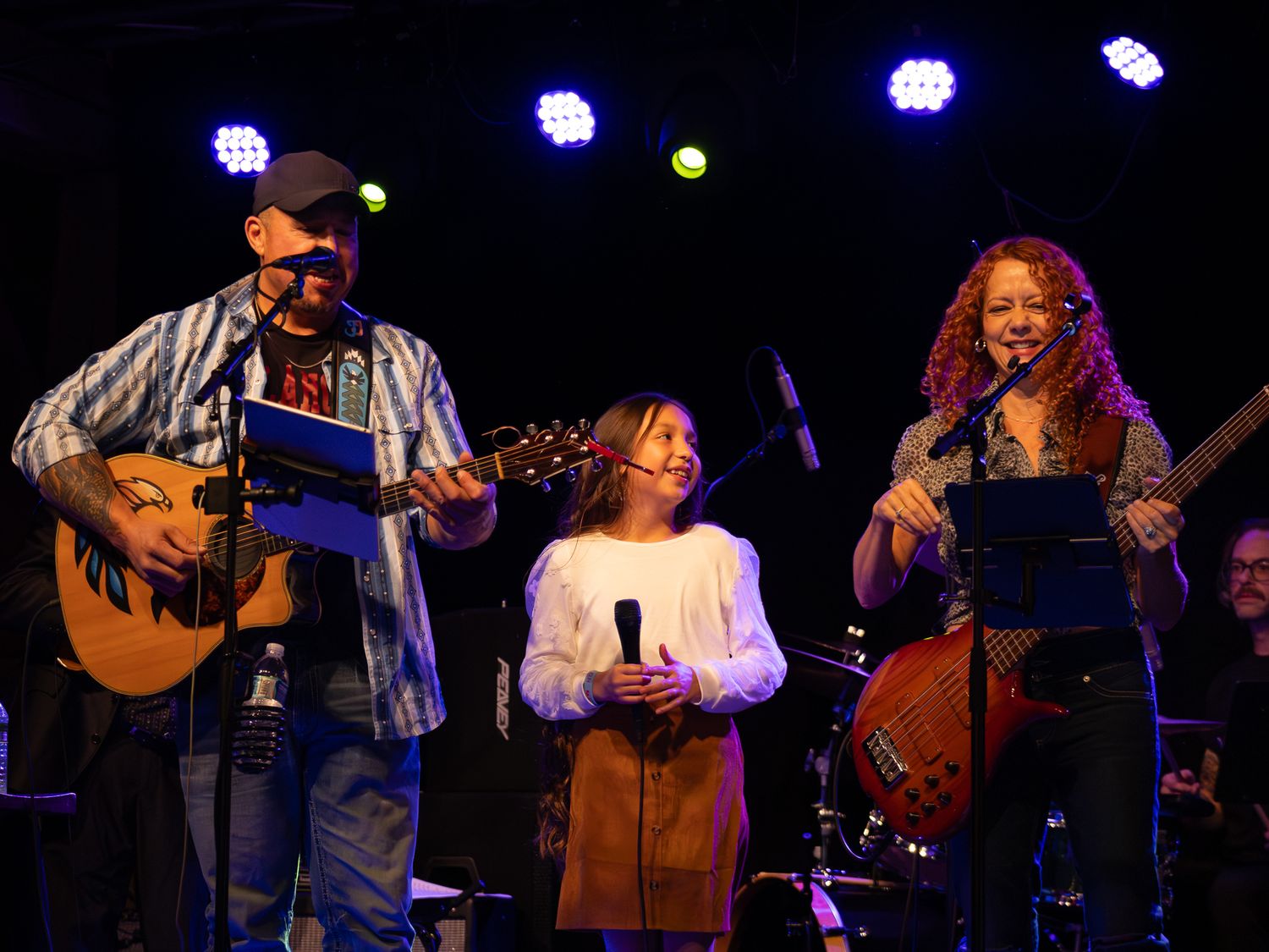 Musicians performing on stage with instruments under blue stage lighting during a live concert.