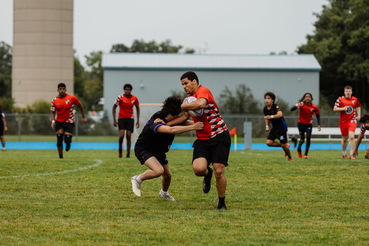 Players compete in an outdoor rugby match on a green field, with one player attempting a tackle during gameplay.