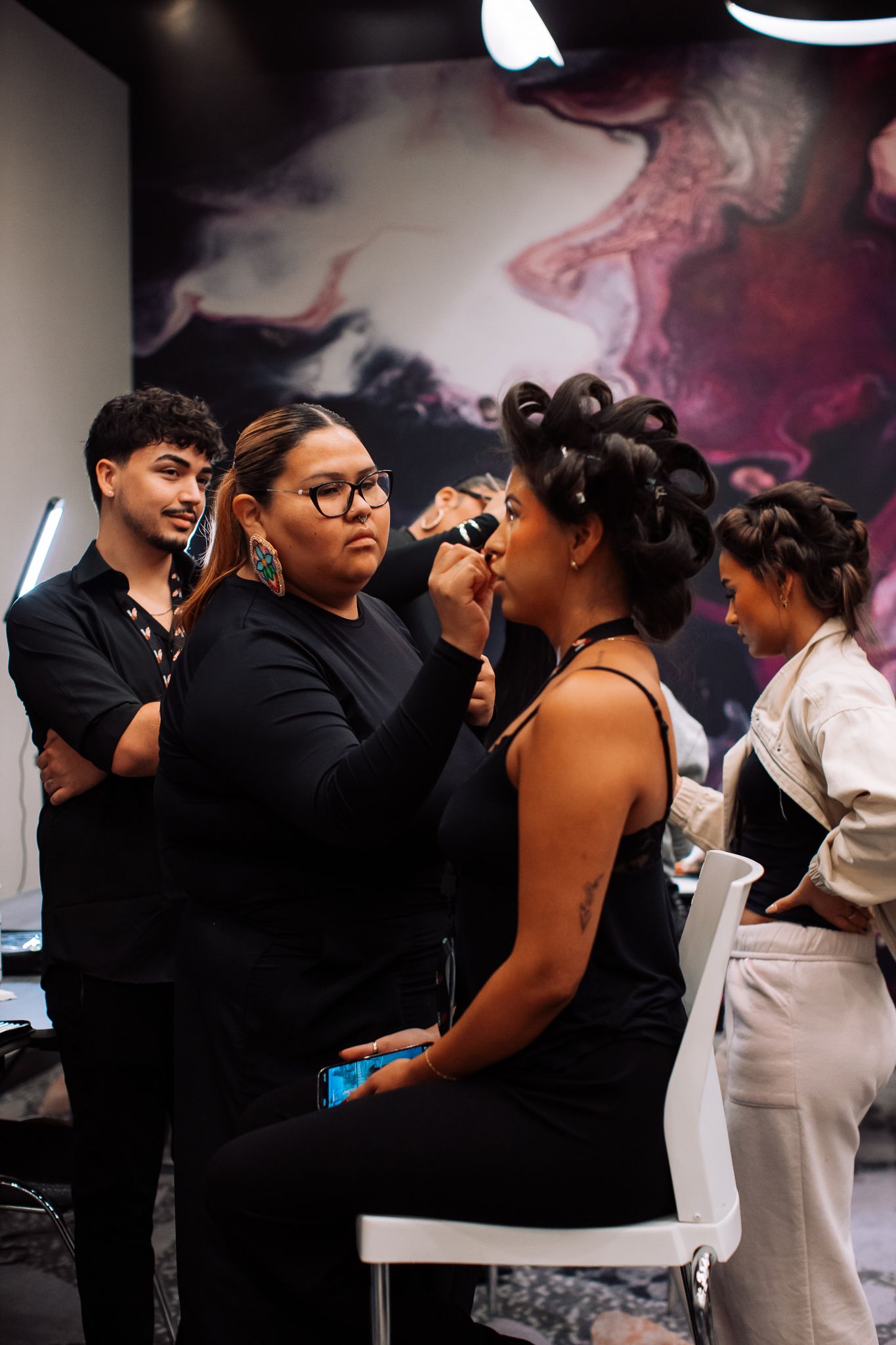 Makeup artist applying cosmetics to a seated client in a modern salon with abstract wall art.