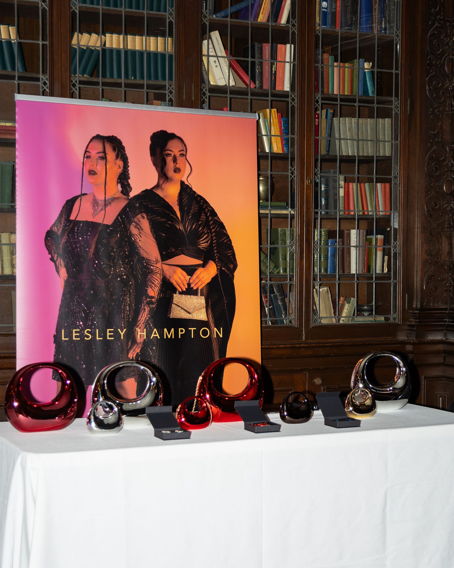 Lesley Hampton fashion display with red and black crystal sculptures and promotional poster in library setting.