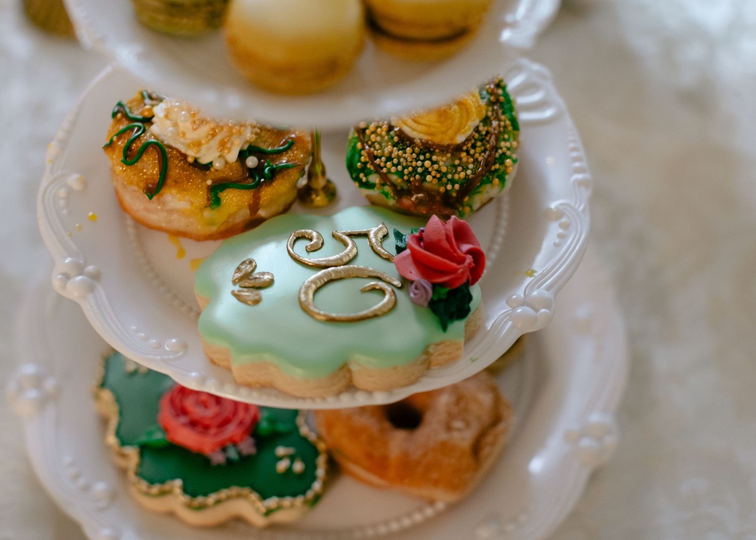 Close-up of ornate decorated cookies and donuts with floral and gold designs on a white tiered serving stand.