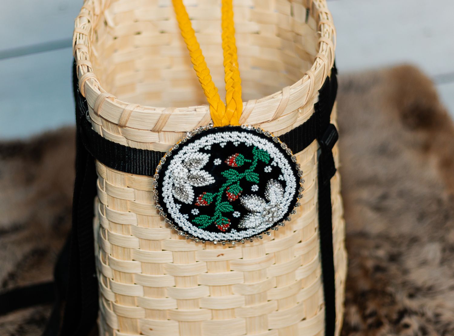 Handwoven basket with beaded floral medallion pendant featuring green leaves and red berries on black background.