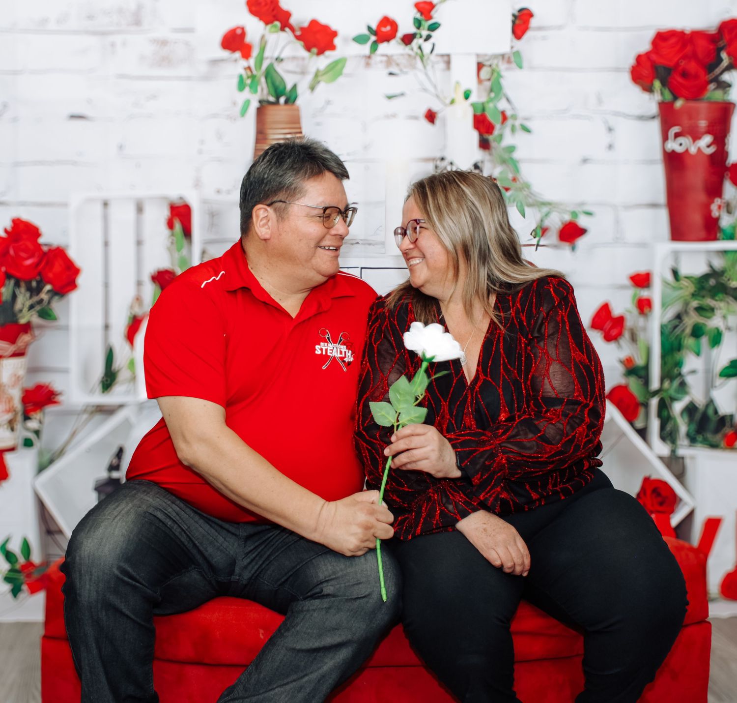 Valentine's themed portrait session with couple posing against decorated white wall with roses.