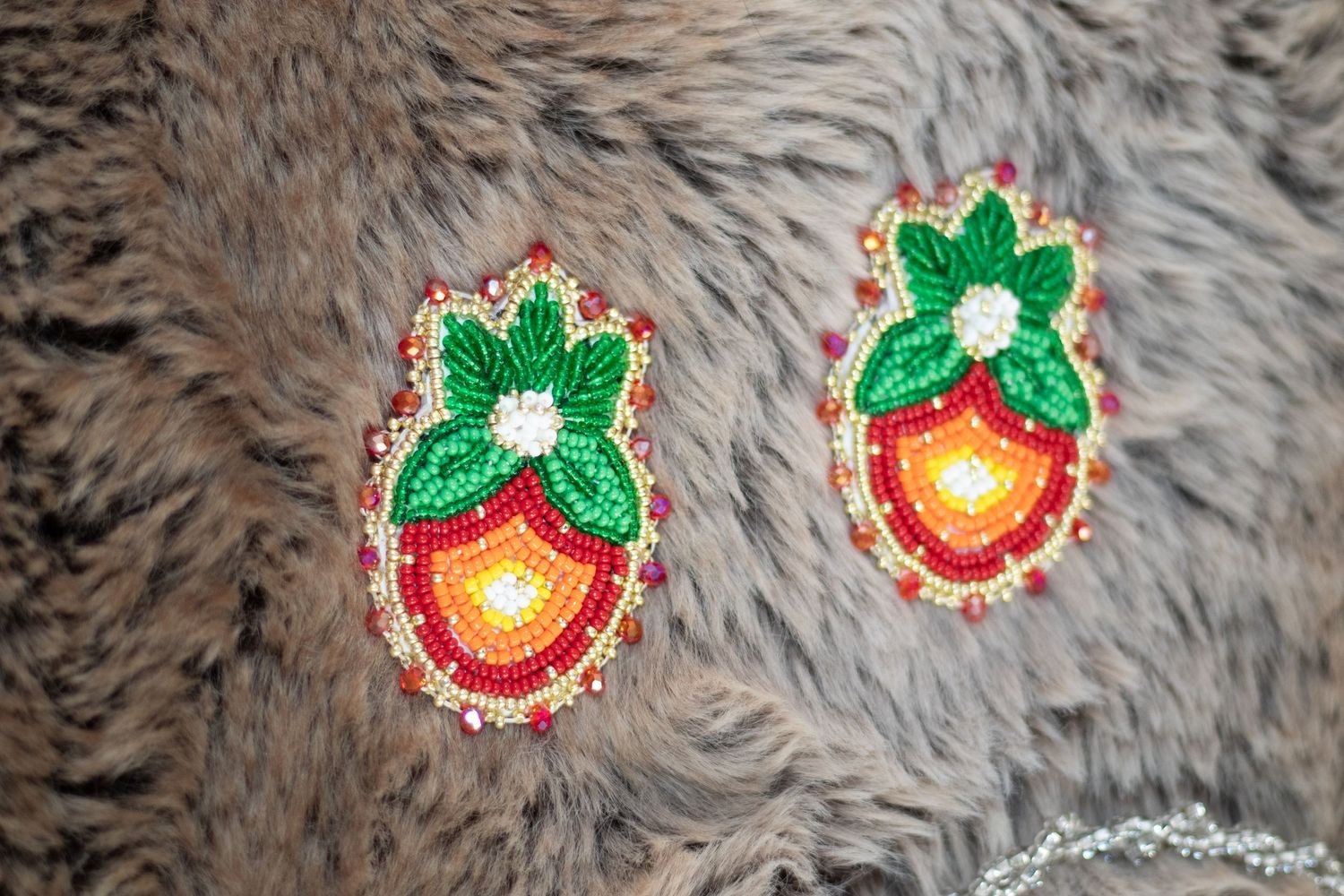 Decorative strawberry-shaped beaded patches with green leaves arranged in a row on fur background.