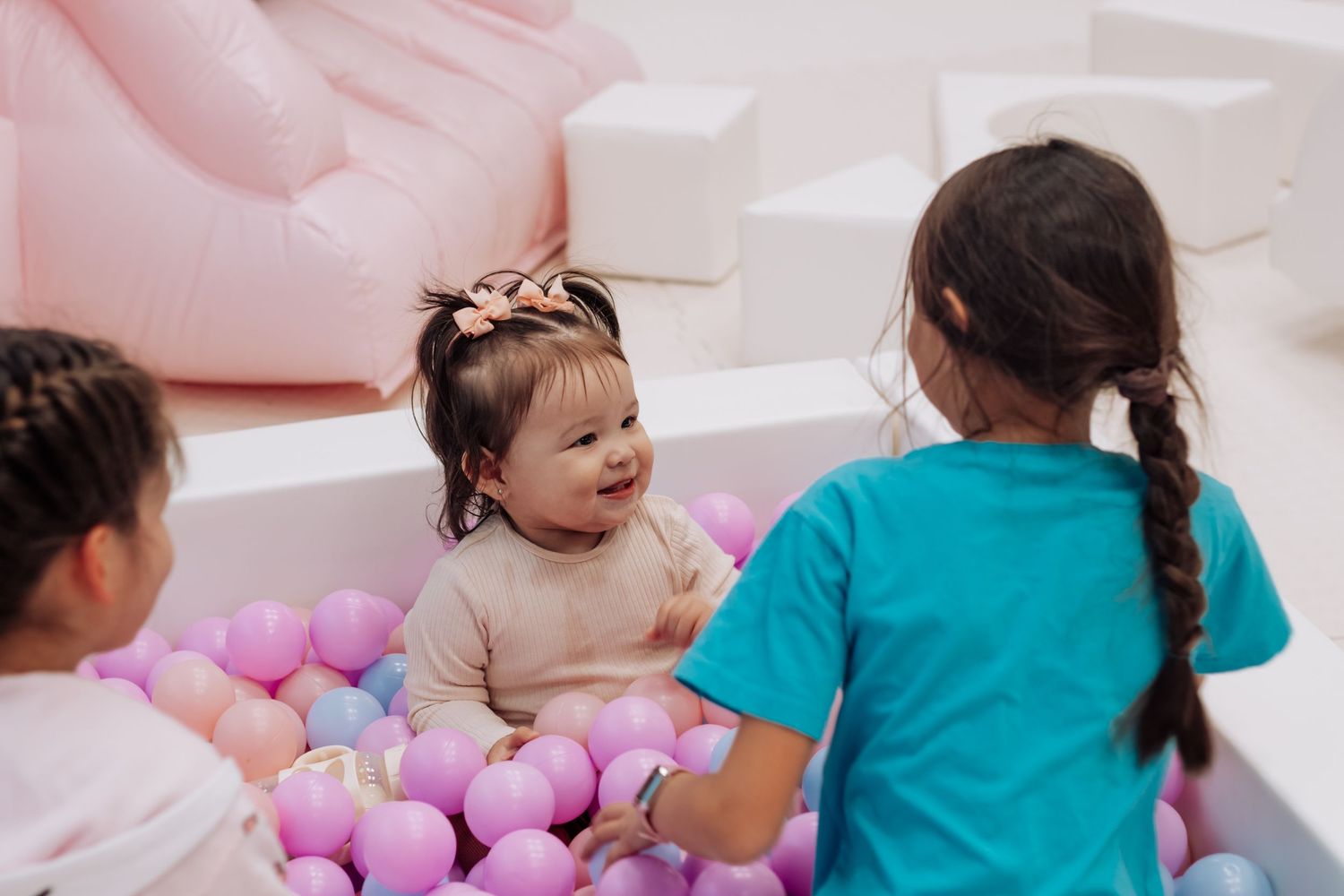 Children playing with pink and purple balloons at a celebration.