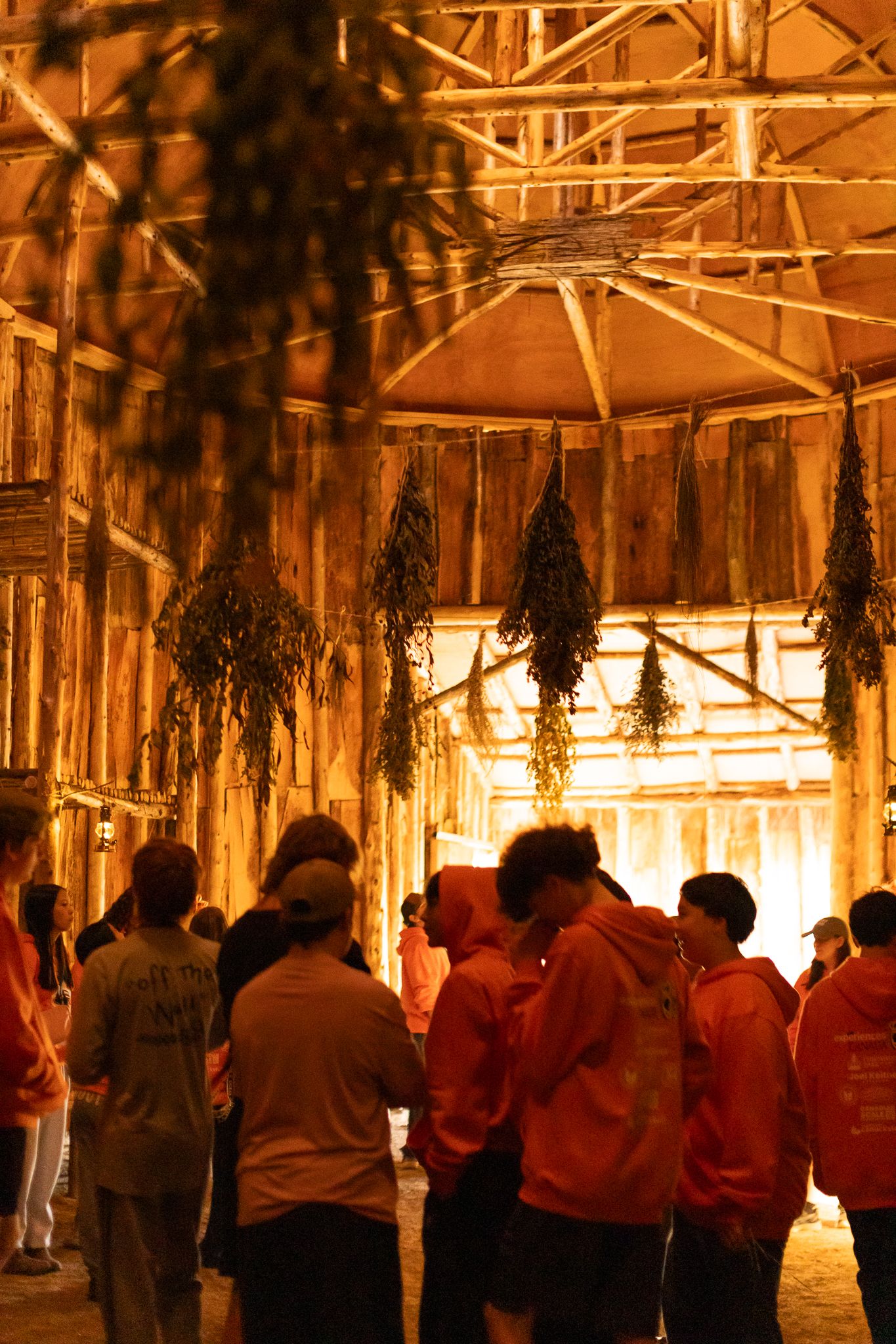 Large group gathered inside rustic wooden structure with hanging decorations.