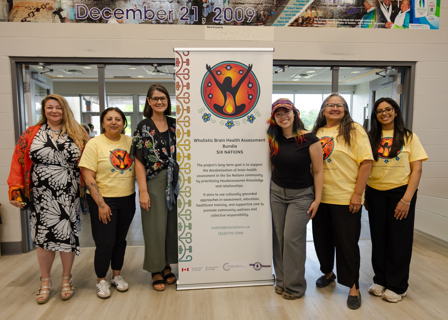 Group of seven women posing together indoors near a mental health awareness banner dated December 21, 2009.