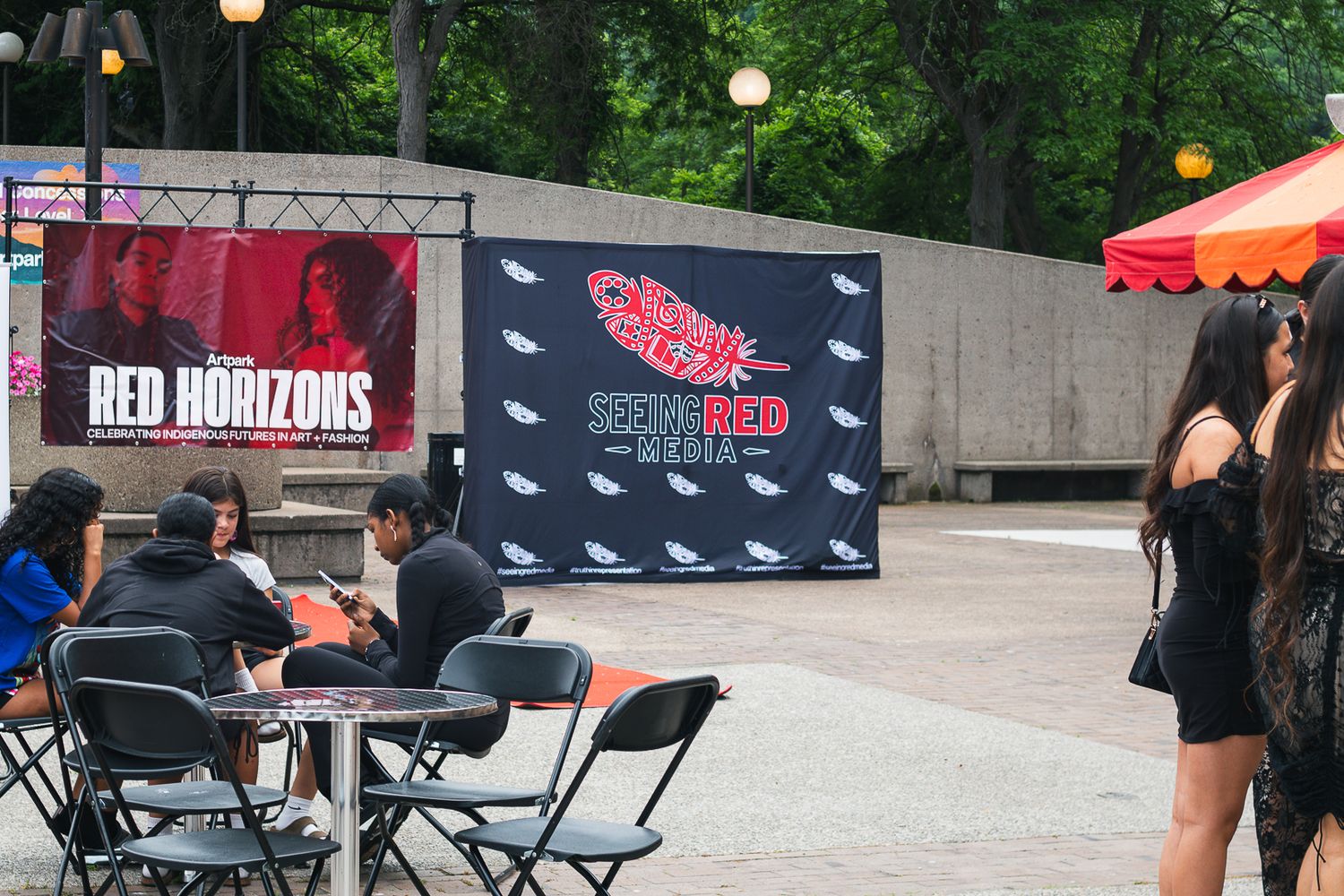 Outdoor event with Red Horizons banner and Seen Red Media backdrop, guests seated at tables in an urban plaza.