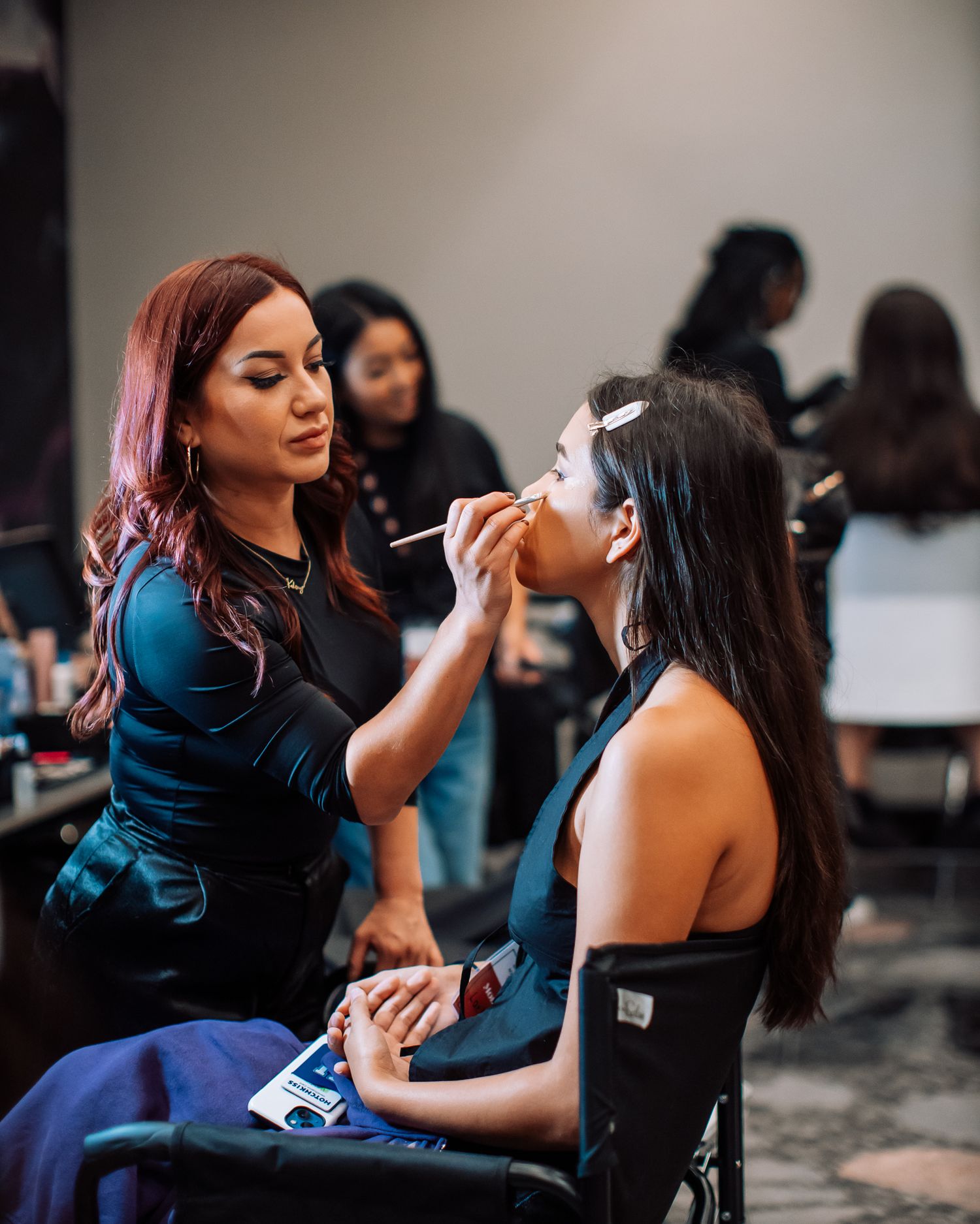 A makeup artist with red hair applies makeup to a young woman at a professional beauty event.