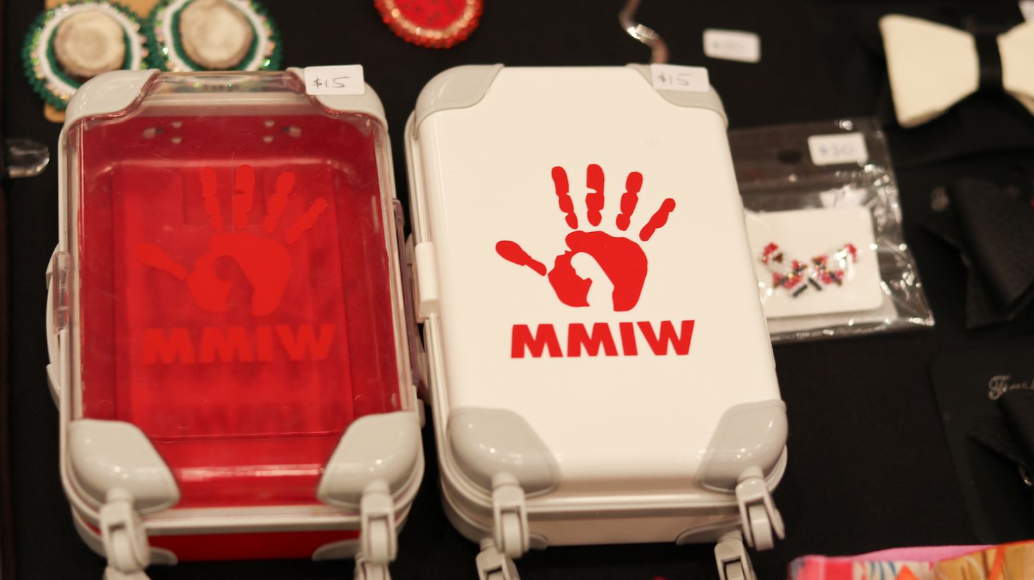 White MMIW cases with red handprint logo displayed on a table with various items at an awareness event.