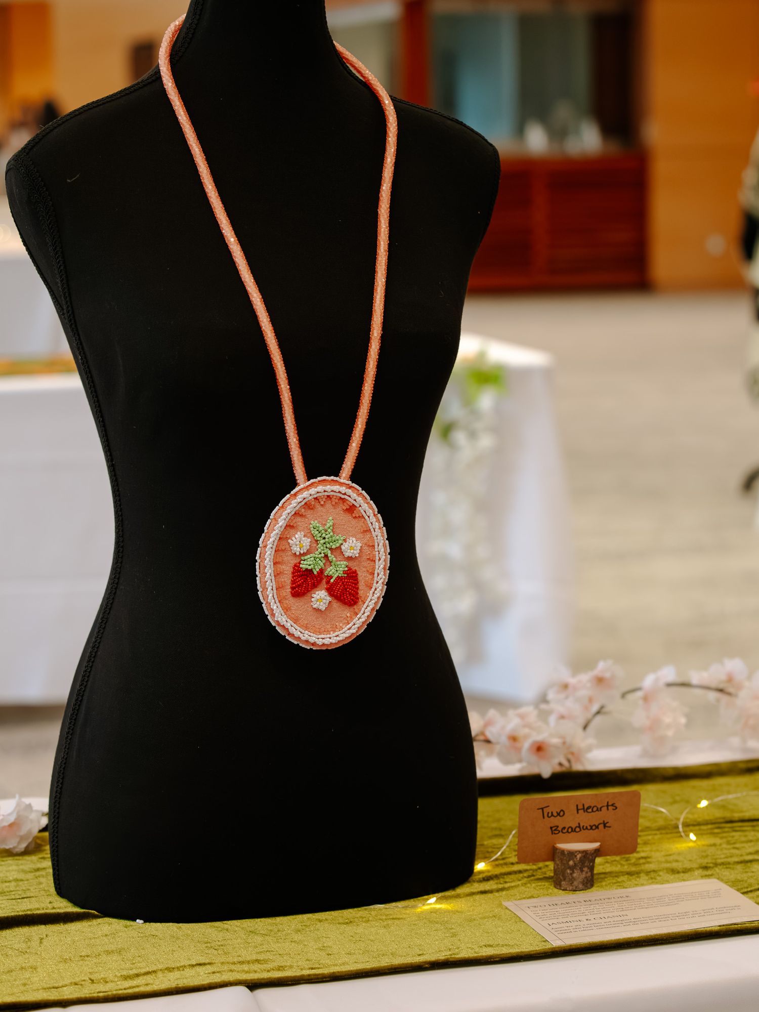 Handcrafted beaded necklace with strawberry motif pendant on black mannequin bust displayed at craft show.