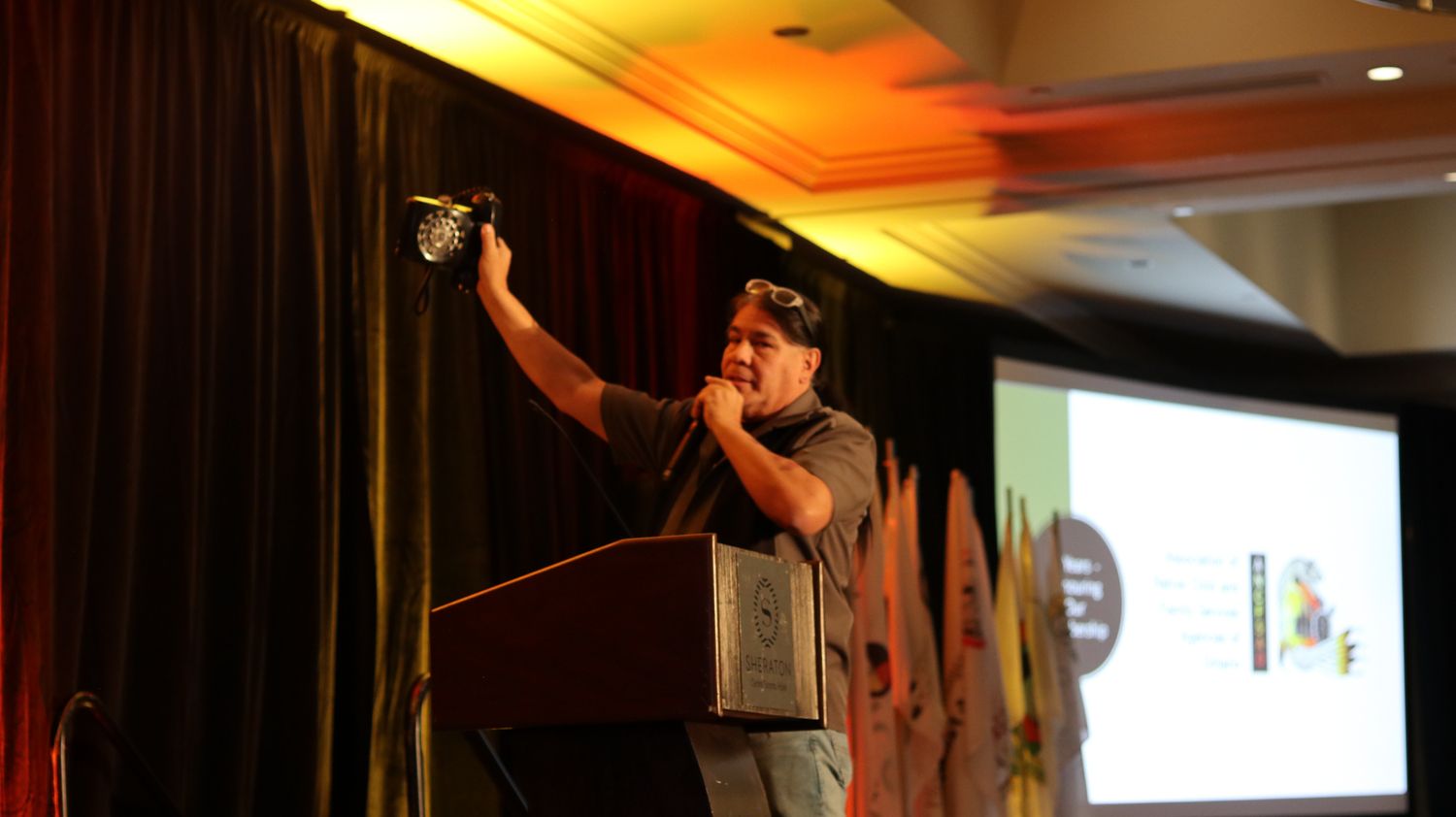 Man holding trophy aloft at podium during awards ceremony in conference hall with presentation screen.