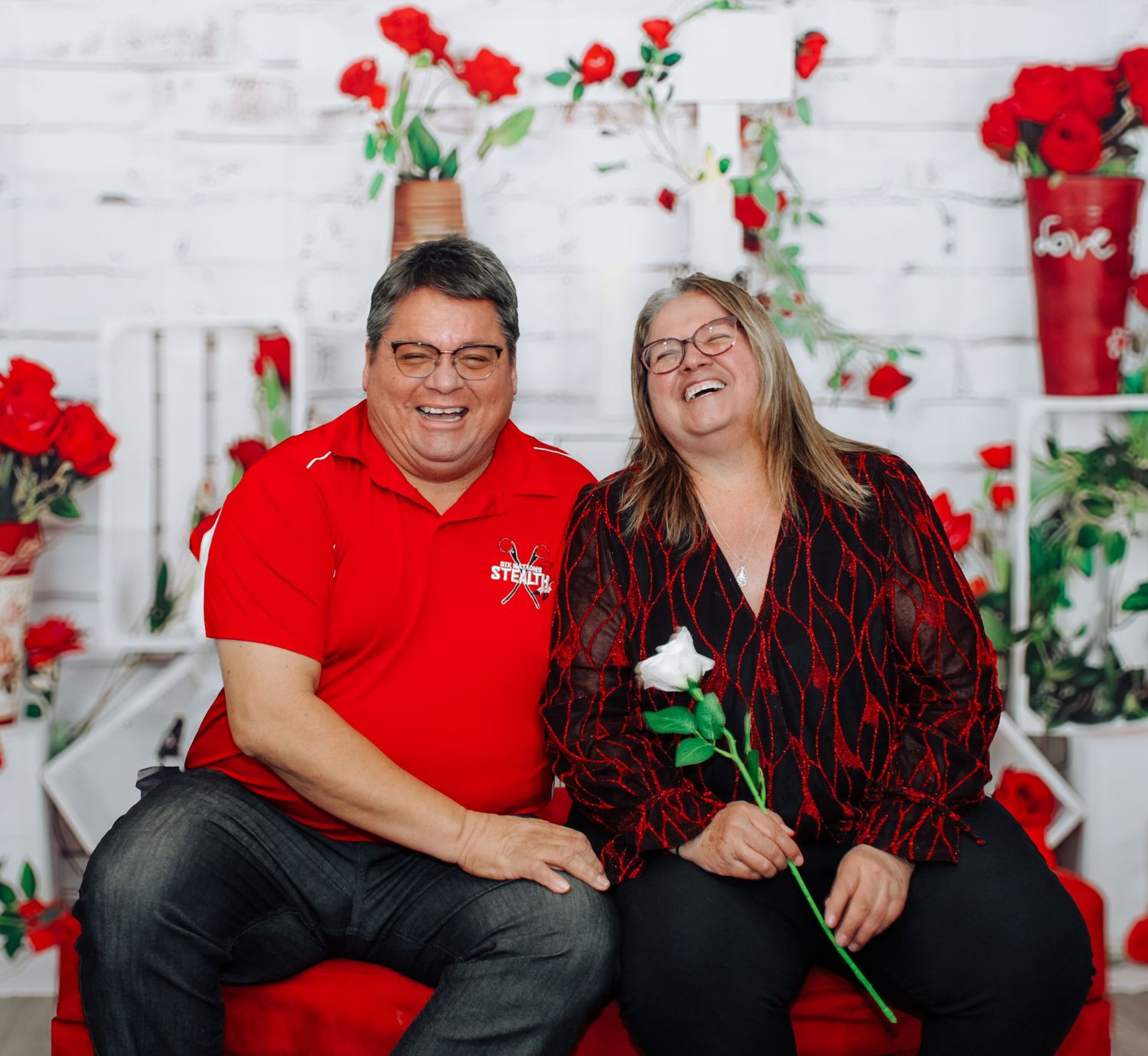 Couple in red and black outfits sharing intimate moment in Valentine's themed photo setting.