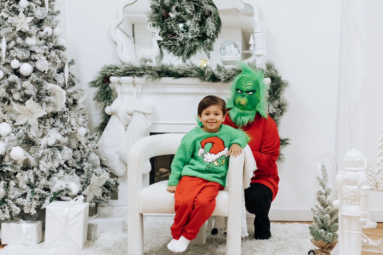 A child sits with someone in a green costume by a decorated Christmas fireplace.
