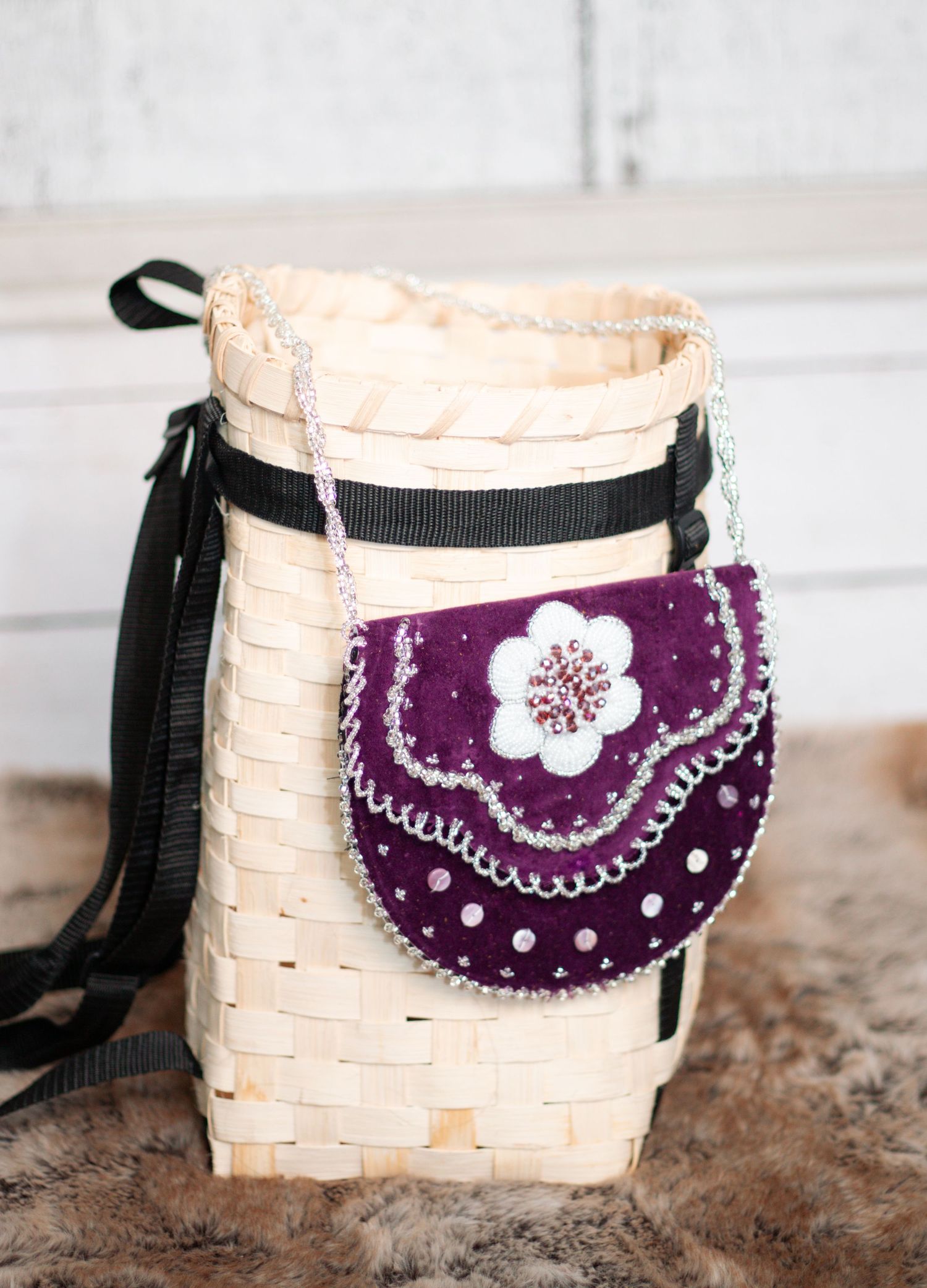 Purple velvet pouches with white floral embroidery displayed on white woven baskets.