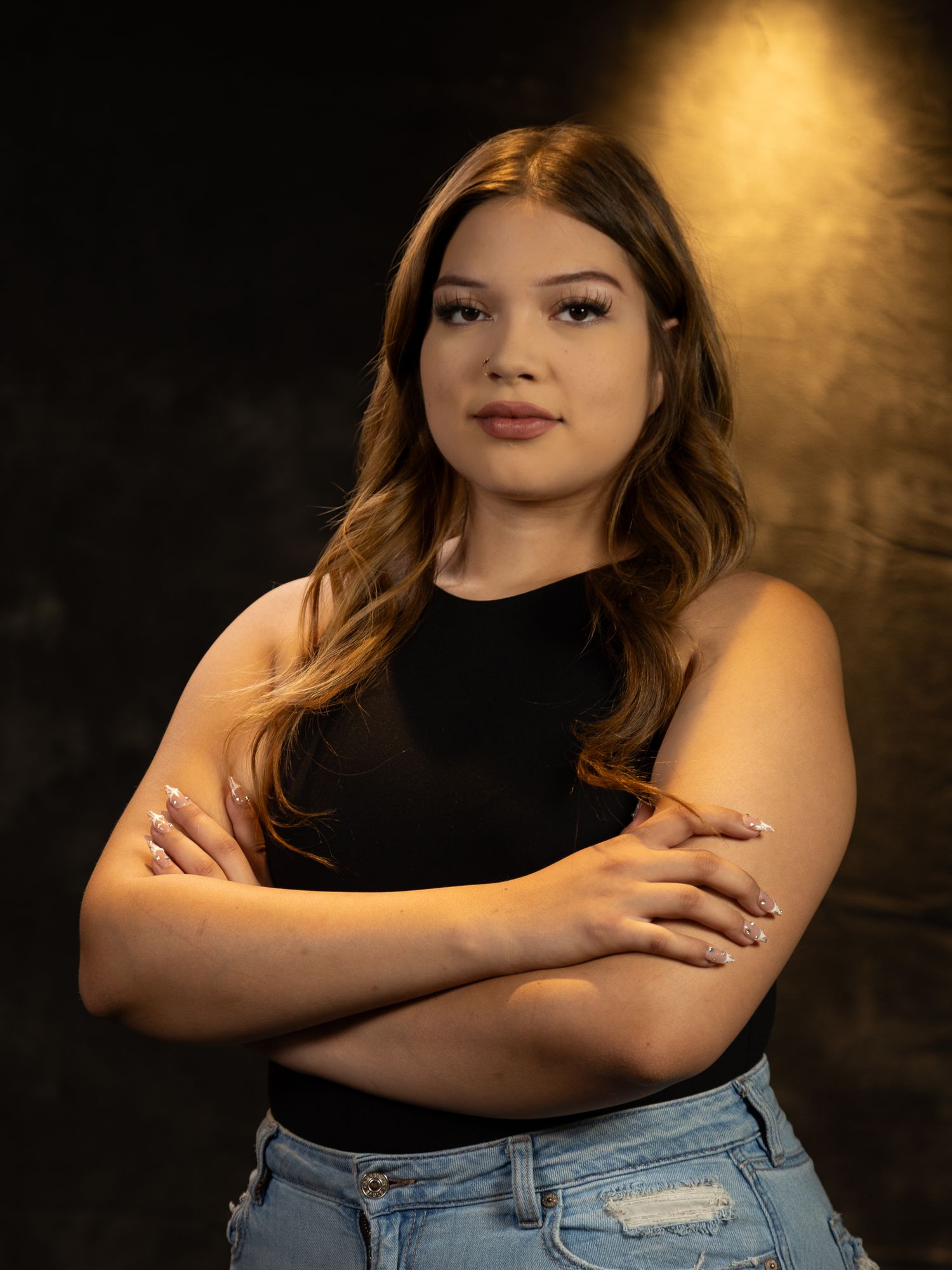 Professional portrait of person in black top with crossed arms against dramatic background.