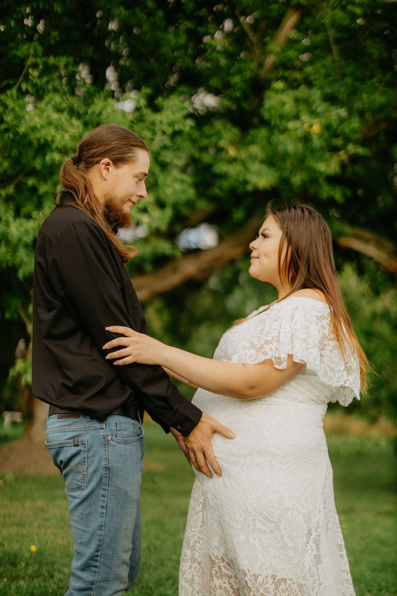 A romantic maternity photo session in a park with green foliage backdrop.