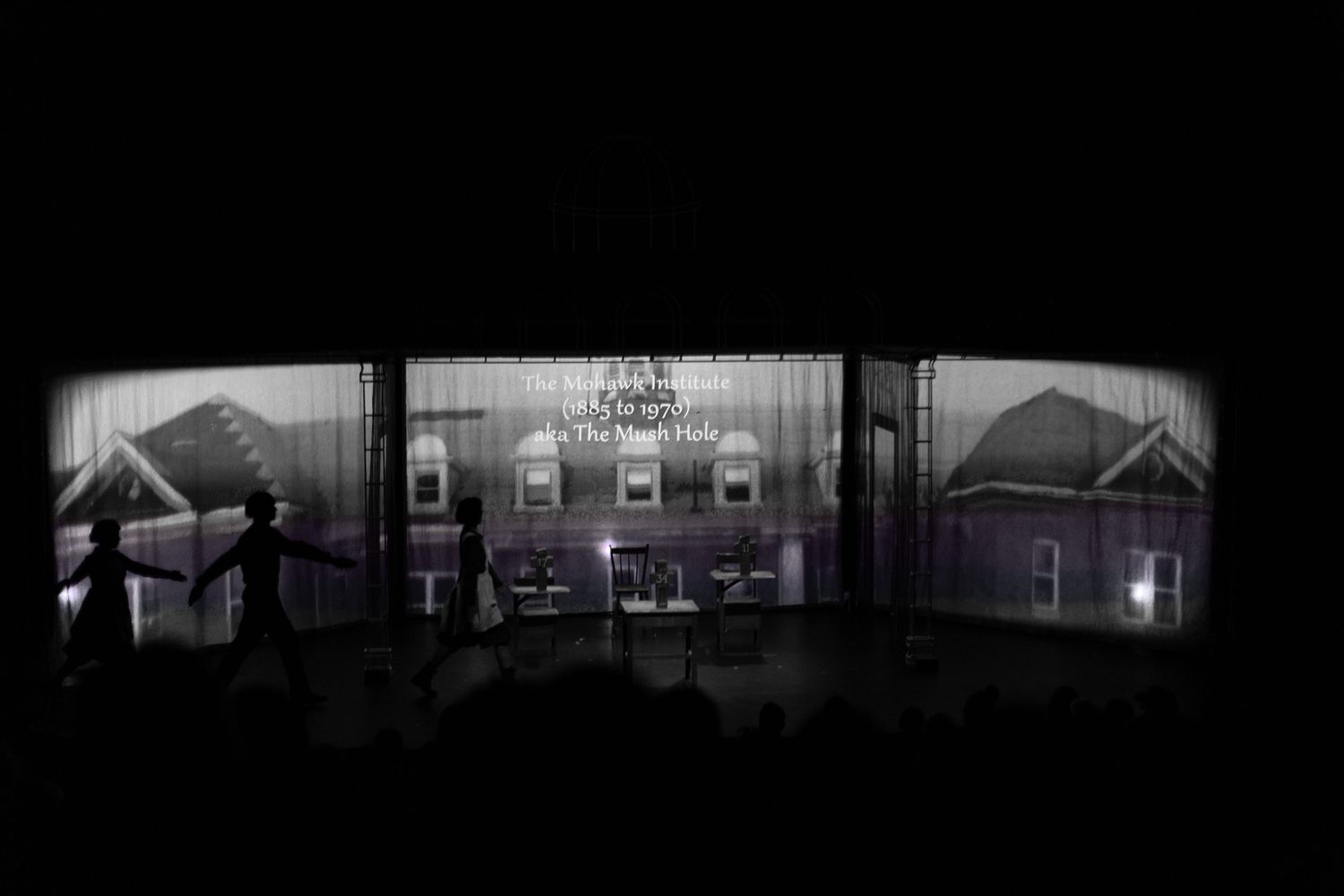 Dramatic silhouette of house structures against illuminated stage backdrop.
