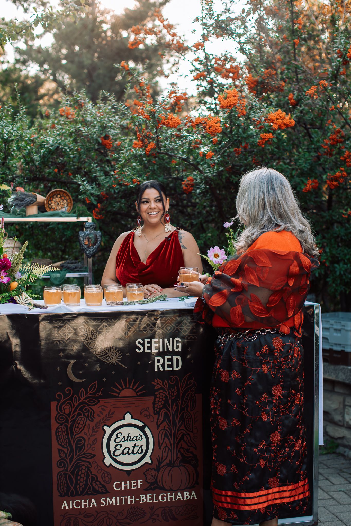 Red-themed outdoor event setup with branded signage and decorative orange berries in background.
