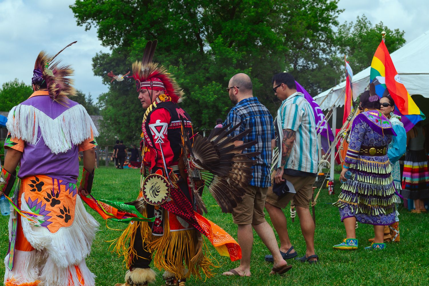 People in traditional Native American regalia dancing at an outdoor powwow celebration.