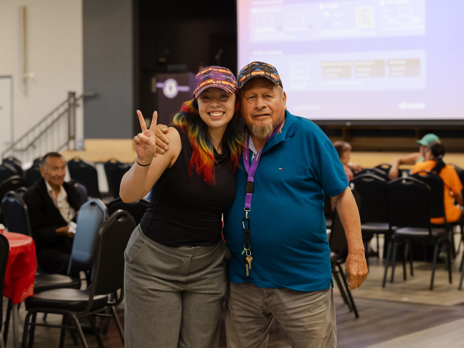 A smiling woman and man pose together making a peace sign at an Indigenous community event.
