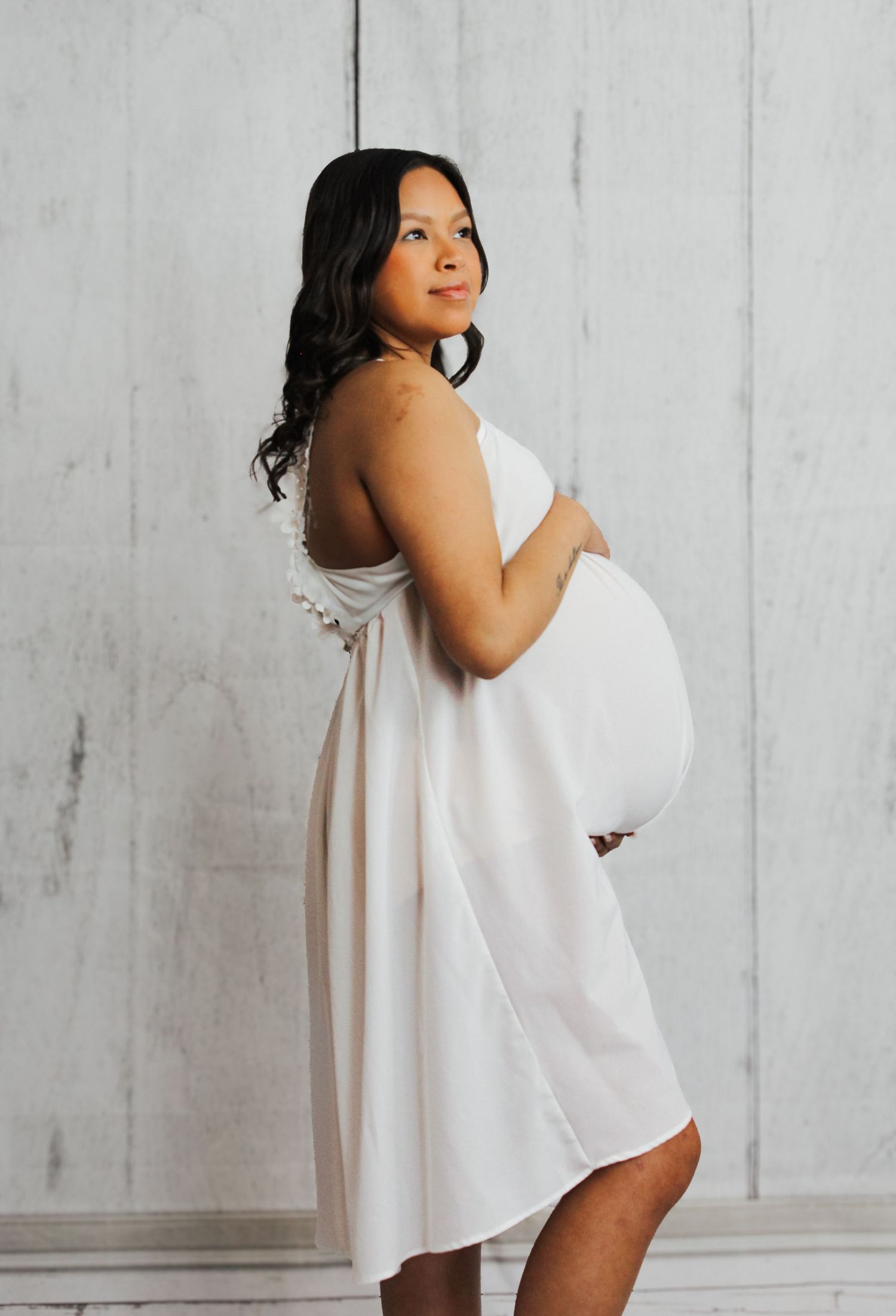 Artistic maternity photo series showing a woman in white against a light gray backdrop.