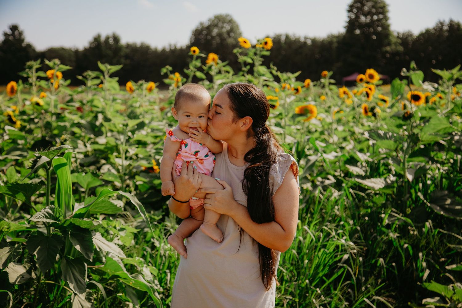 Sweet candid moment shared between parent and baby in a field of towering sunflowers.