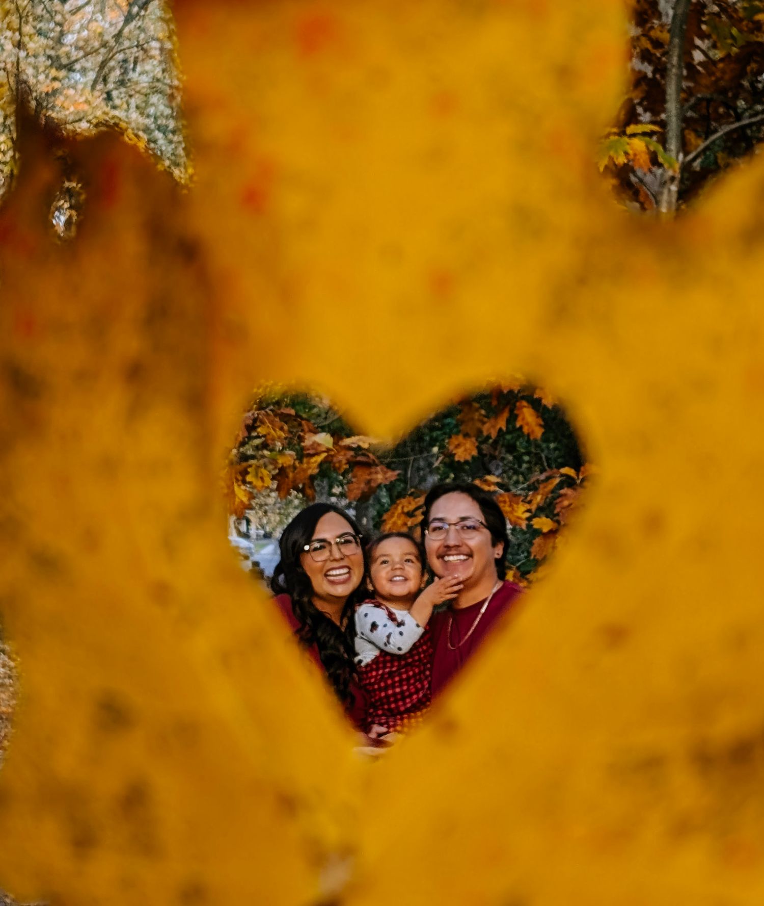 Creative family portrait framed through heart-shaped autumn foliage.