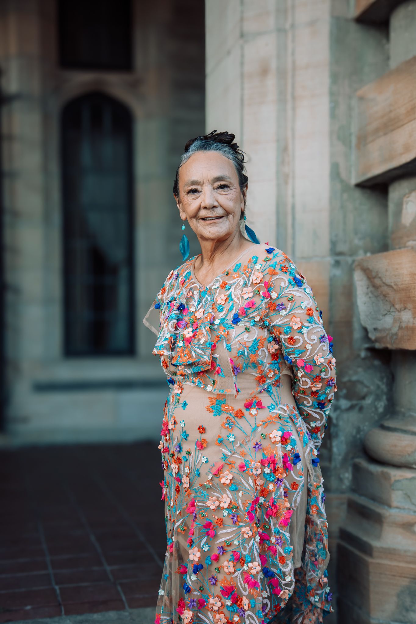 Person wearing colorful floral dress with ruffled sleeves against stone building backdrop.