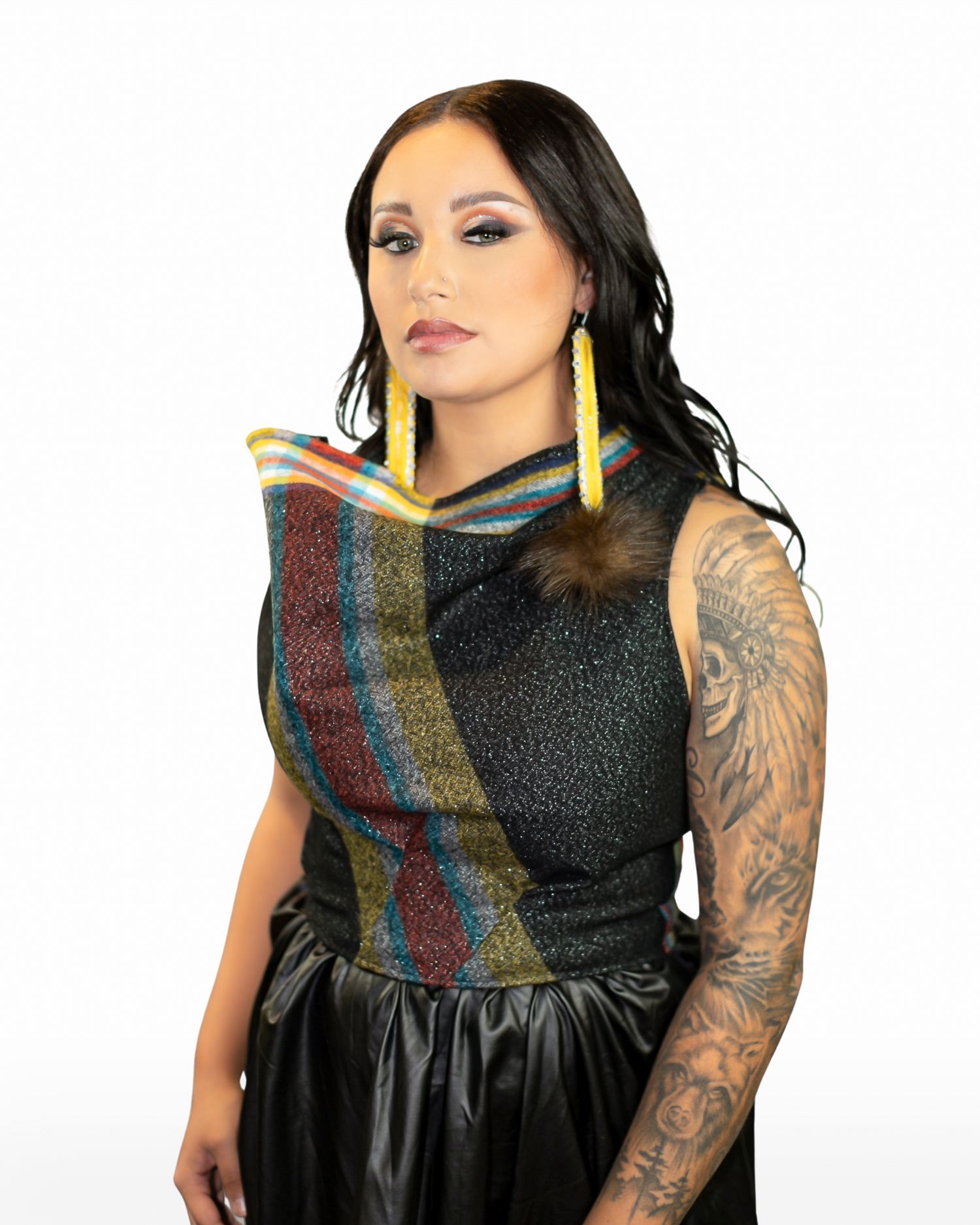 Woman in black sparkle top with colorful stripe detail, yellow beaded earrings, and tattoo sleeve poses confidently.