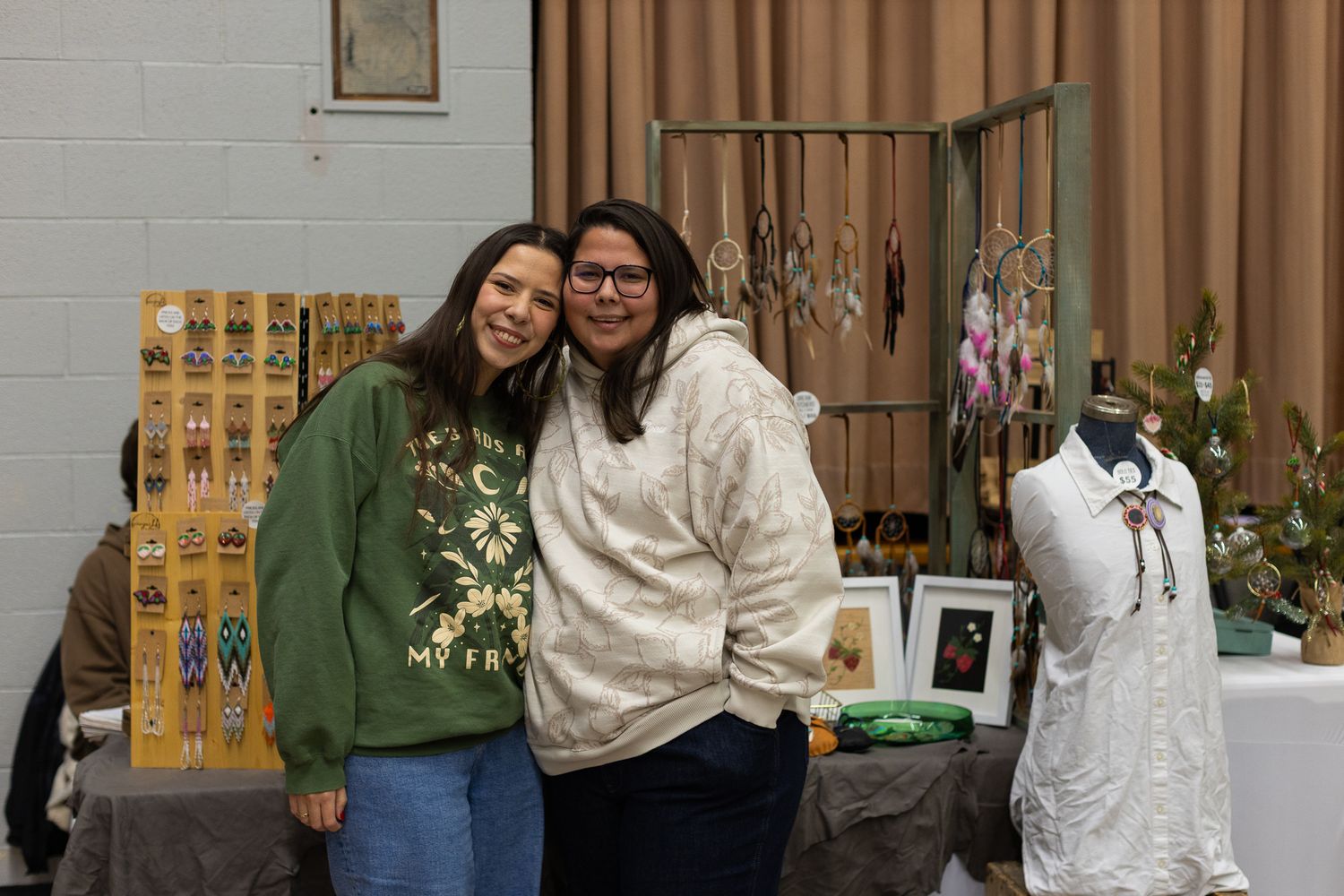 Craft vendors showcasing their work at tables against a gray wall with brown curtains.