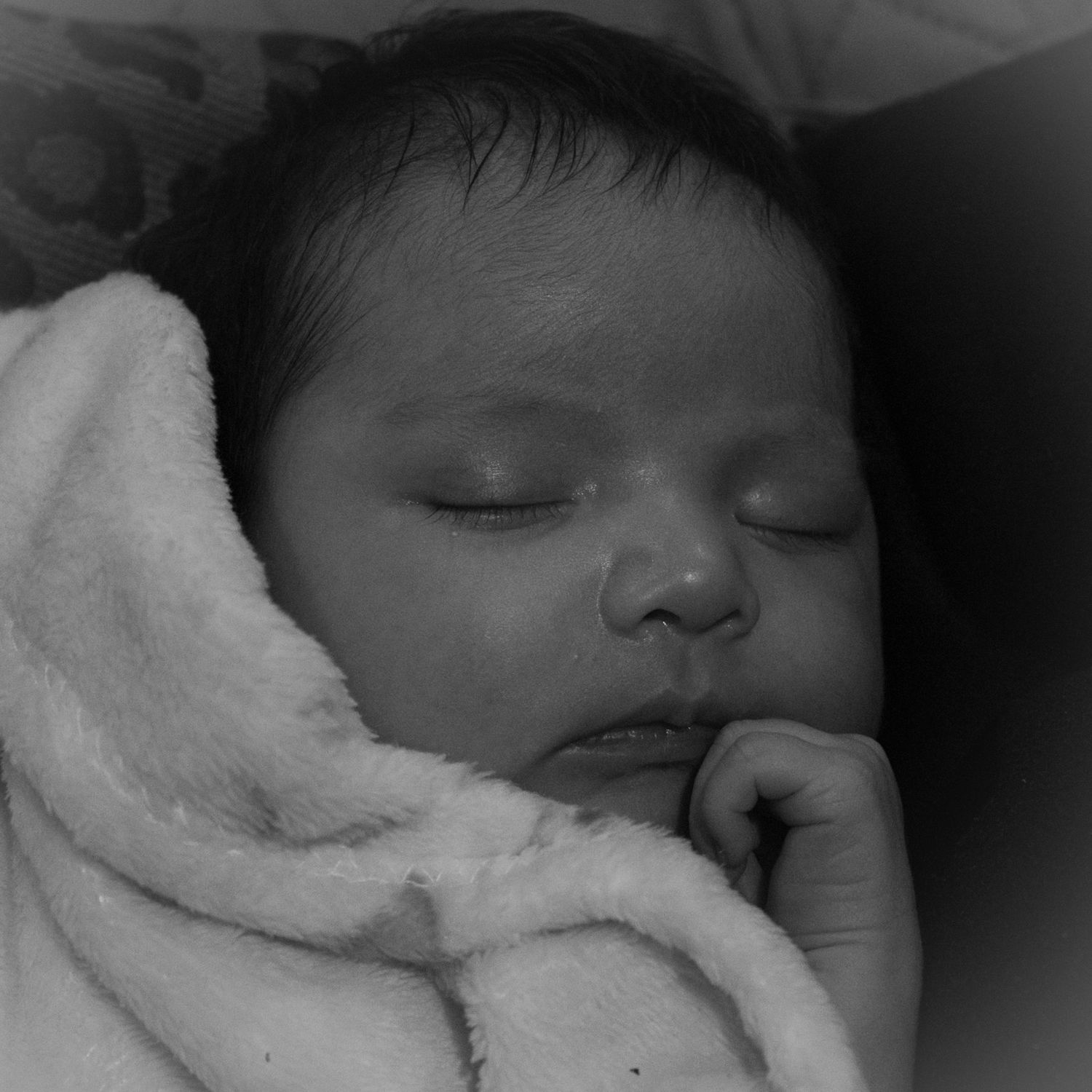 Black and white close-up of sleeping infant wrapped in soft blanket.